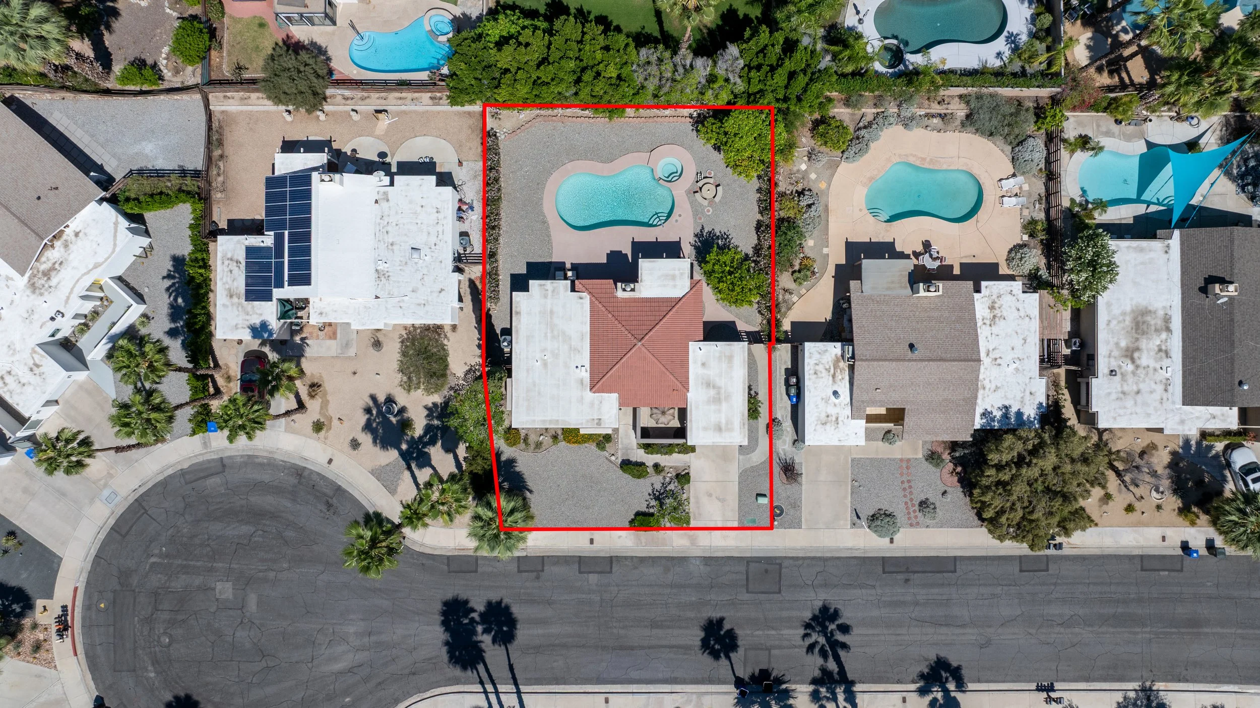 Aerial view of a residential backyard with a swimming pool, hot tub, and landscaping, outlined by a red border.