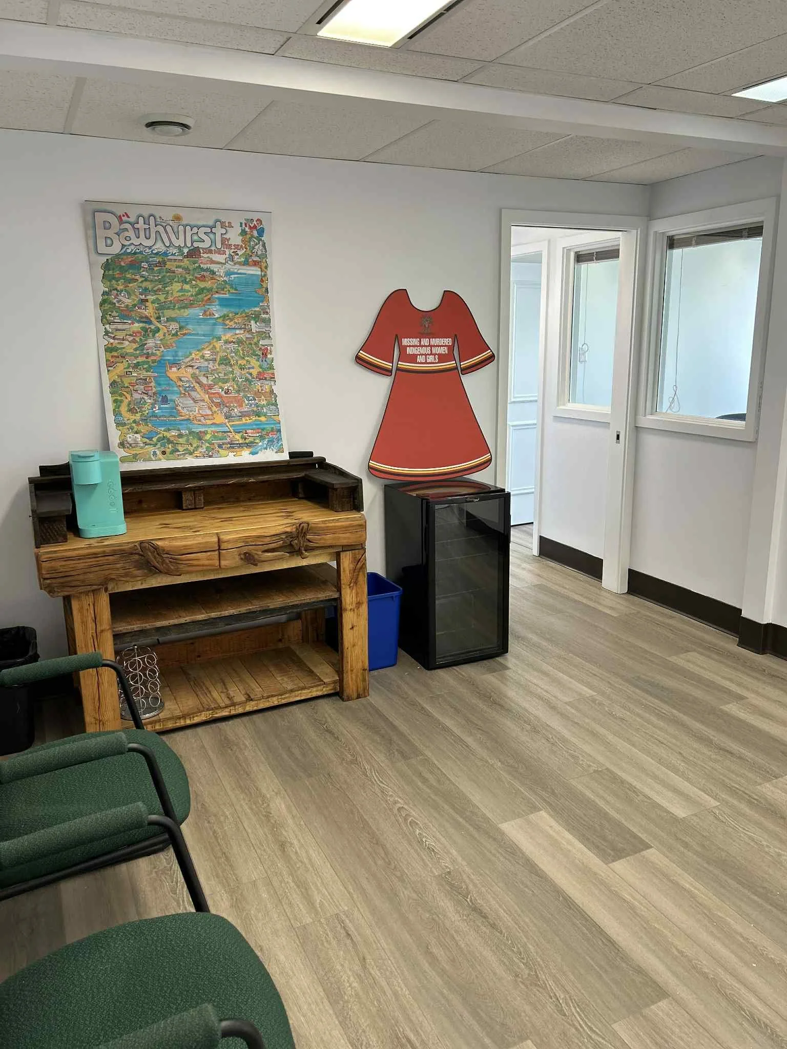 Empty room with green chairs, a wooden counter, a map poster, and a red dress cutout on the wall.