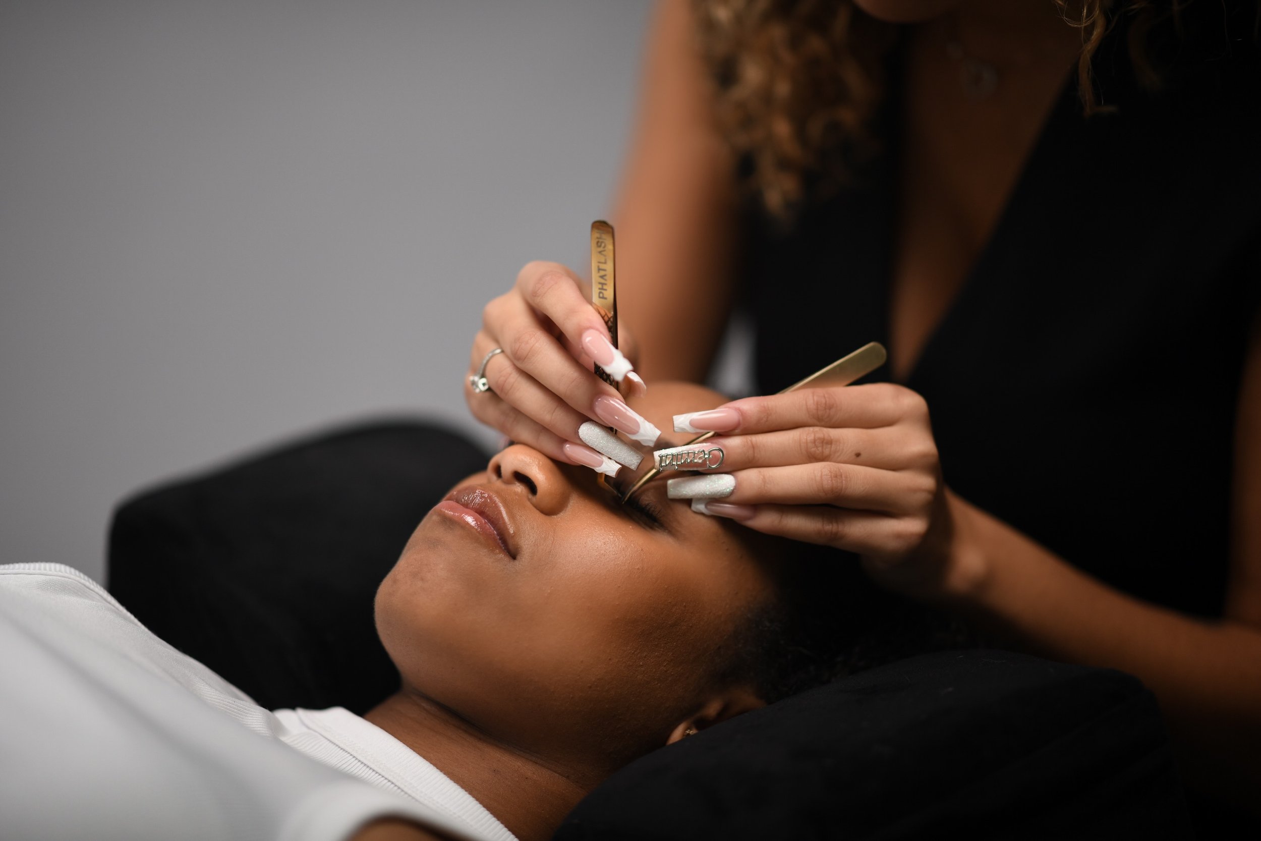 A woman receives eyebrow threading from a professional stylist in a salon or spa setting.