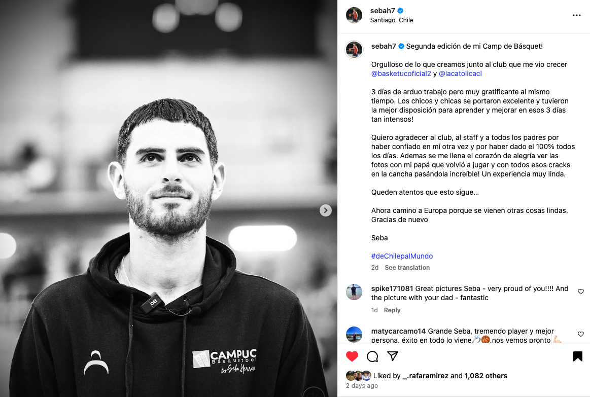 Joven con barba y camiseta con logo de campamento de baloncesto en un gimnasio, fondo desenfocado en blanco y negro.
