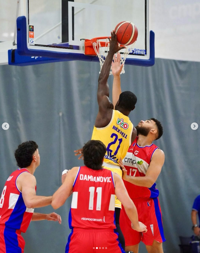 Jugadores de baloncesto en acción durante un partido, con dos en el aro luchando por la pelota y otros dos observando