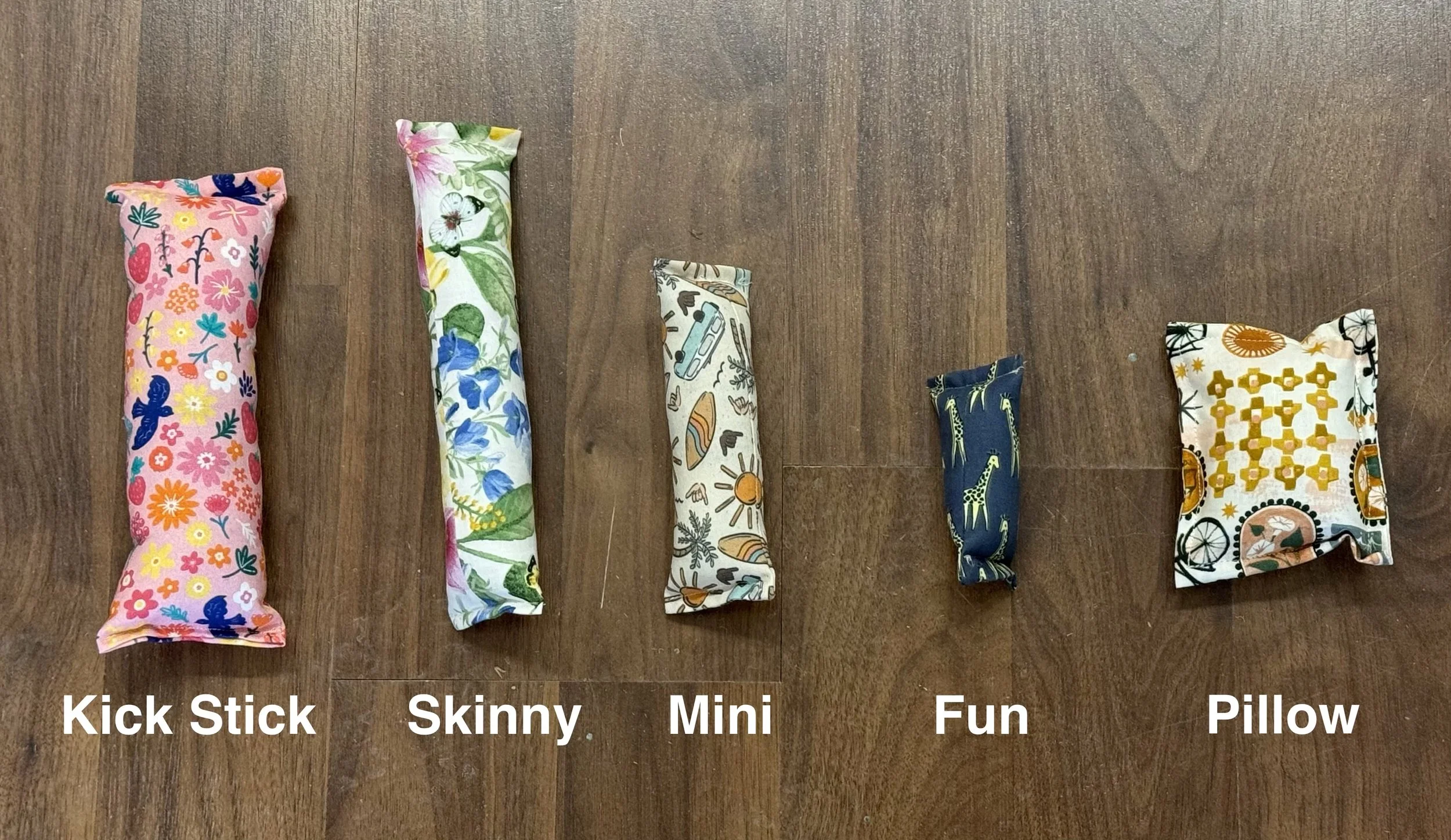 Five handmade catnip toy sizes displayed side by side on wood floor labeled Kick Stick, Skinny, Mini, Fun, and Pillow.