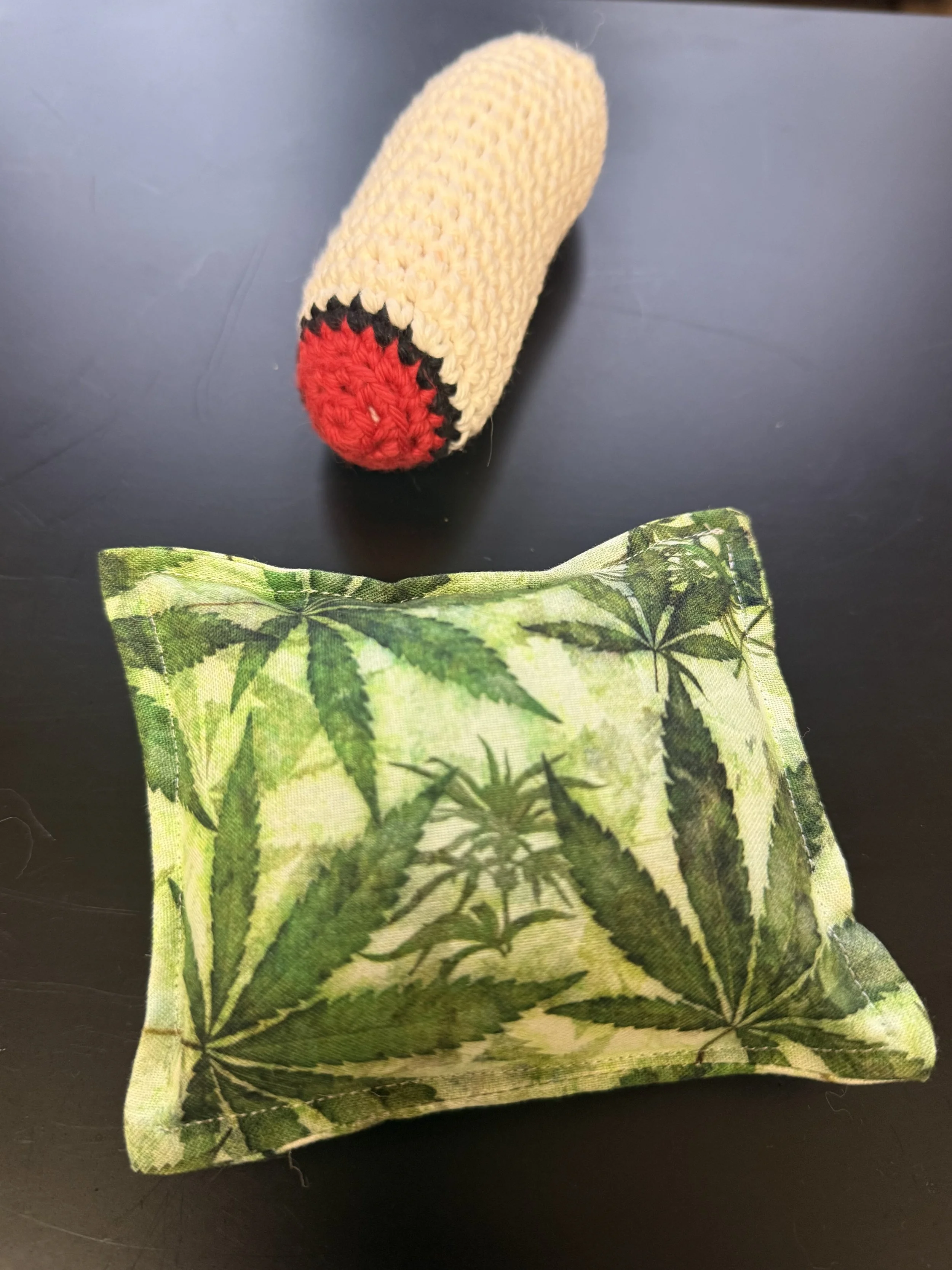 Crocheted catnip joint toy and cannabis leaf print catnip pillow, handmade cat toys displayed on a dark background.