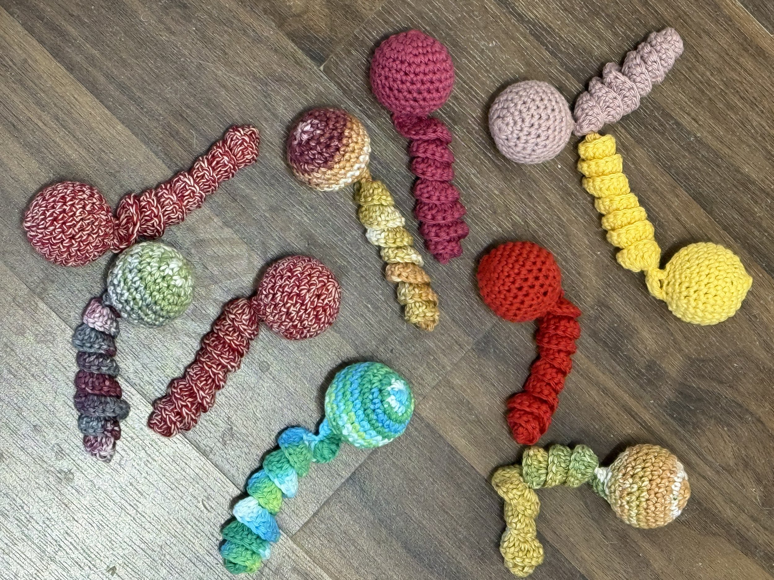 Assortment of colorful handmade crocheted catnip jellyfish toys with round heads and spiral tentacles, laid out on a wooden floor.