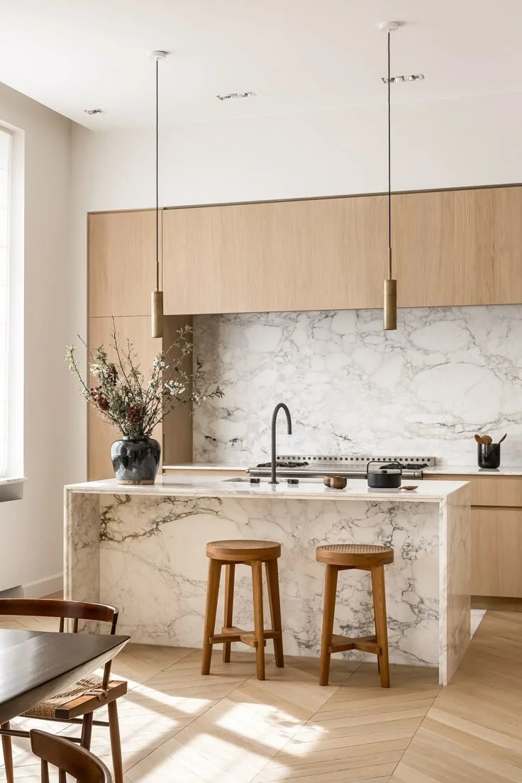Modern kitchen with marble island and backsplash, wooden cabinetry, two pendant lights, and two wooden bar stools.