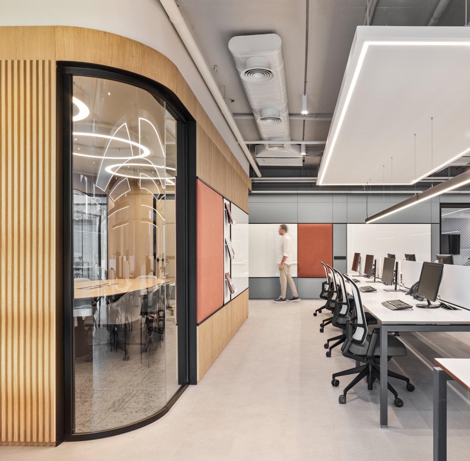 Modern office with a row of computers and a person walking in the background.