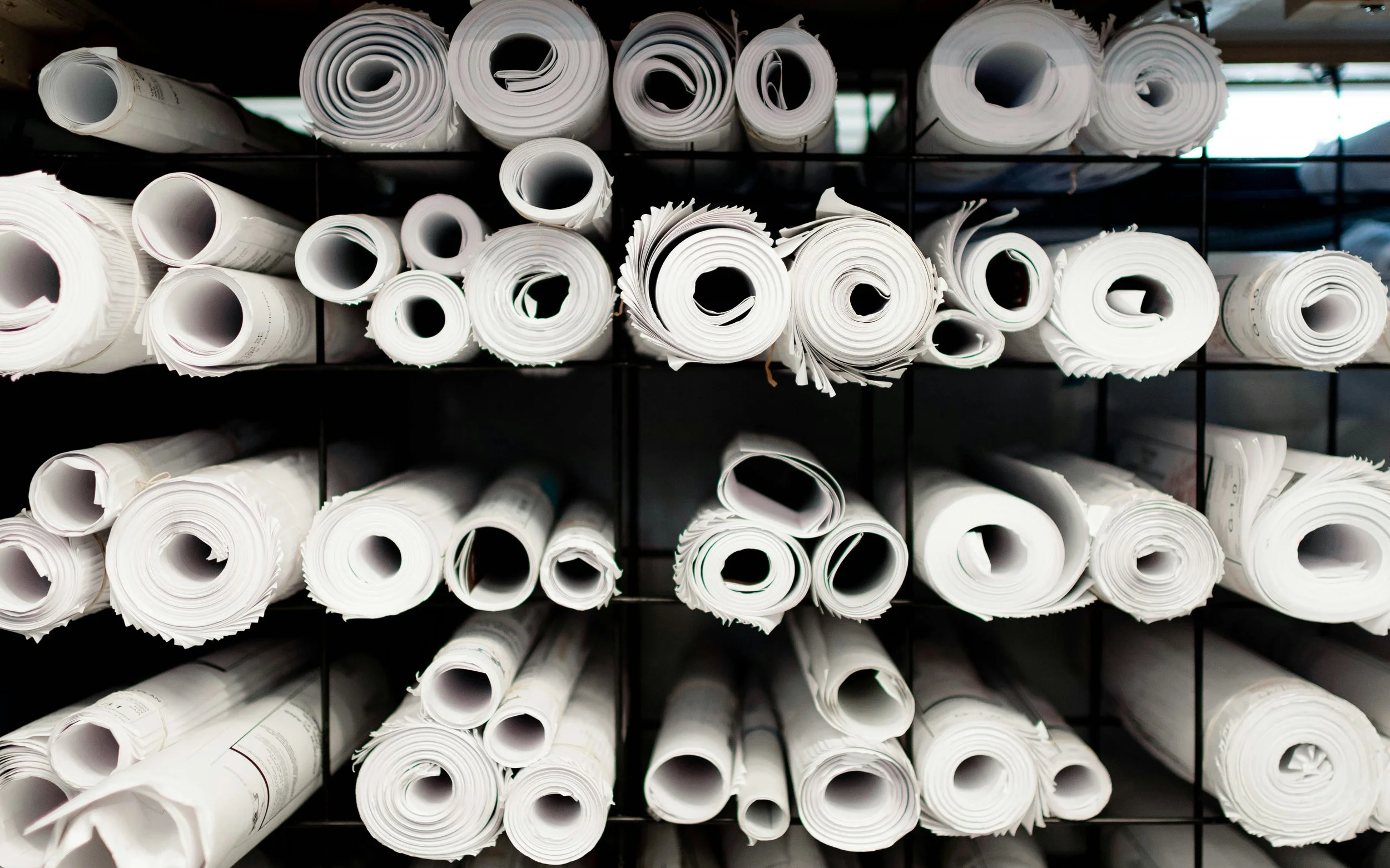 Stacks of rolled-up white architectural permit drawings or large sheets of paper stored on a black metal shelving unit.