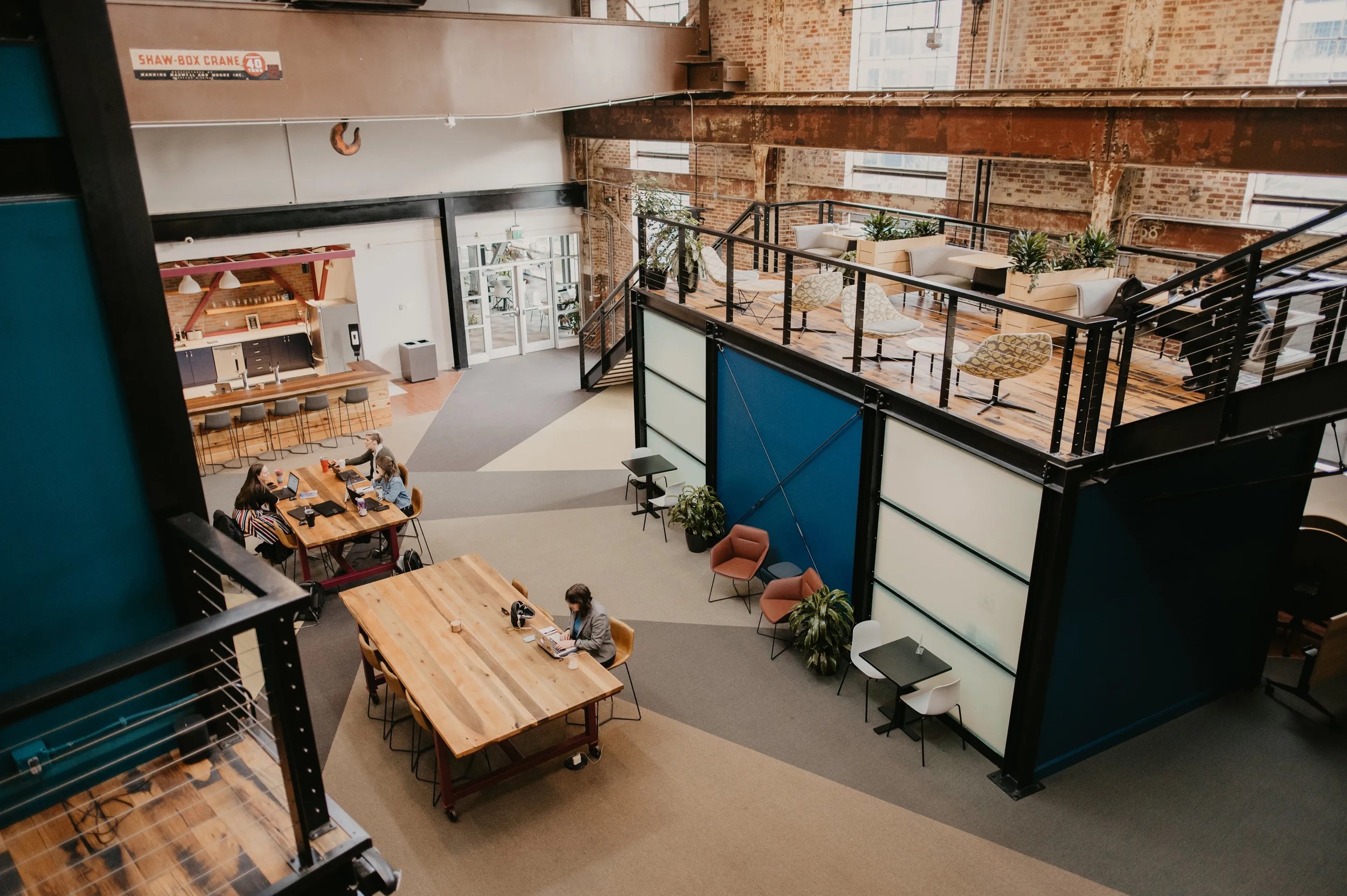 Interior of a modern, open-concept coworking space with multiple seating areas, plants, and exposed brick walls.