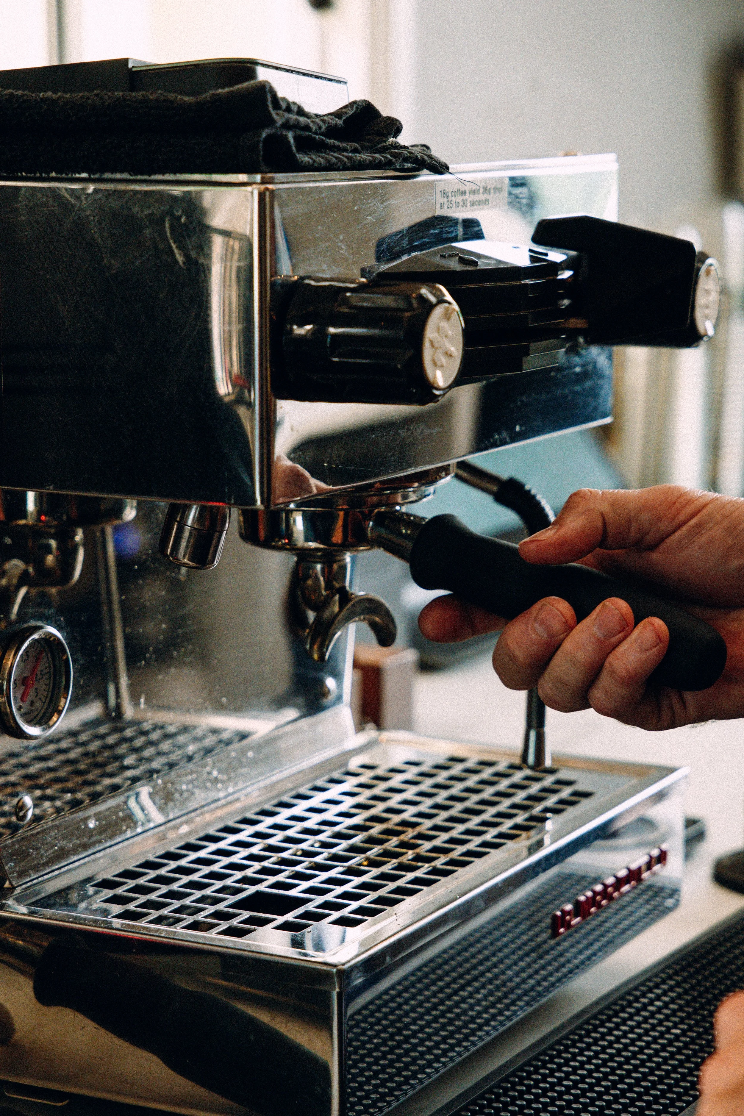 Close-up of a person operating a stainless steel espresso machine, with a black portafilter handle in hand.