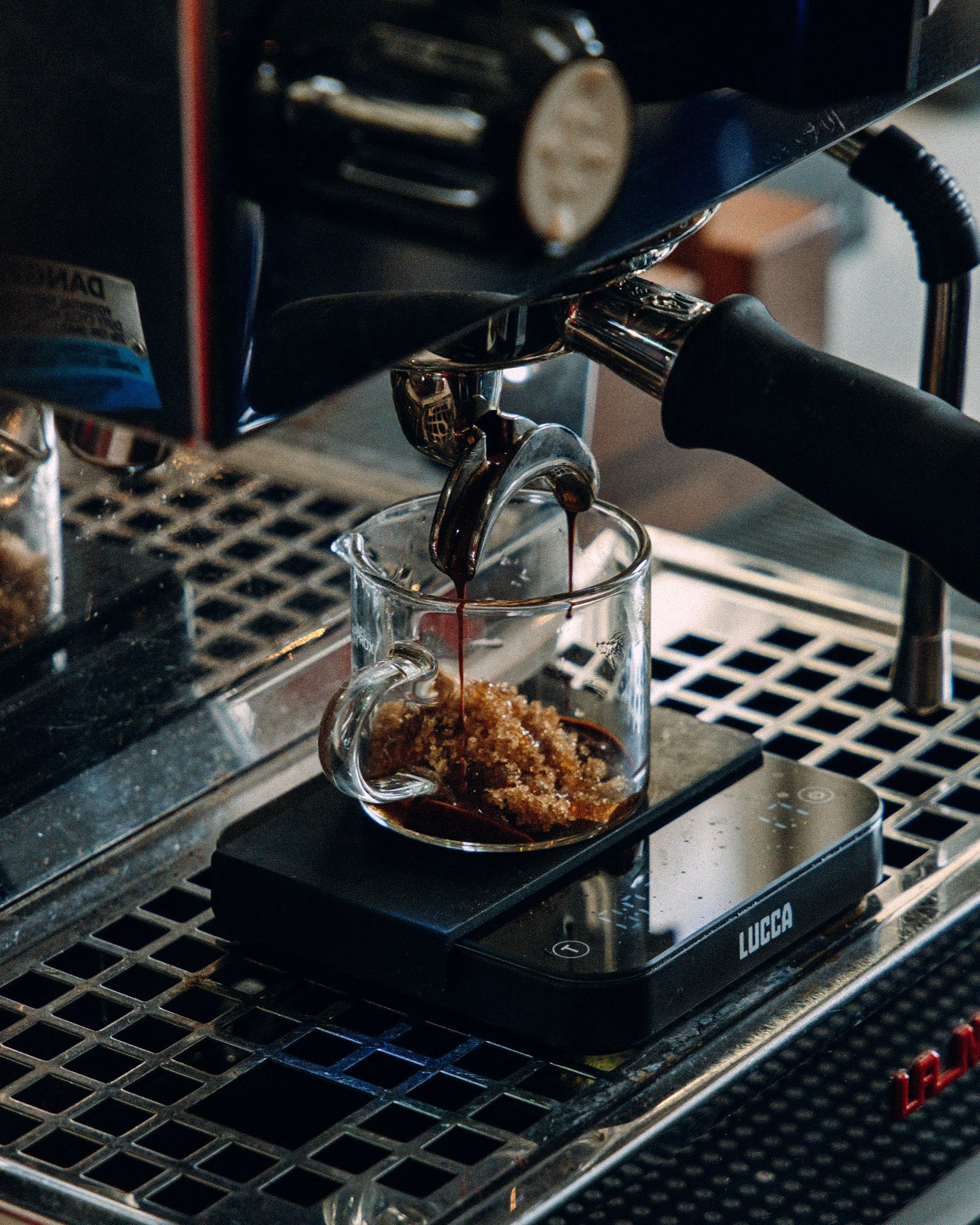 Espresso shot being poured into a clear glass cup from a portafilter in a coffee machine.