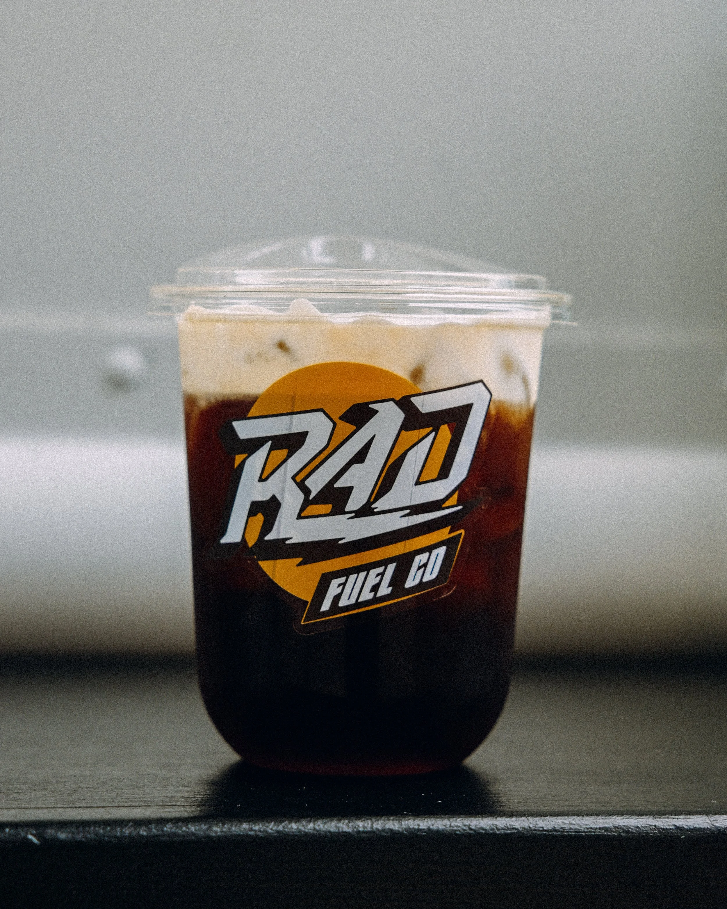 A plastic cup with a black straw, filled with a coldbrew, and a partially visible label with the words 'RAD FUEL CO' on it.