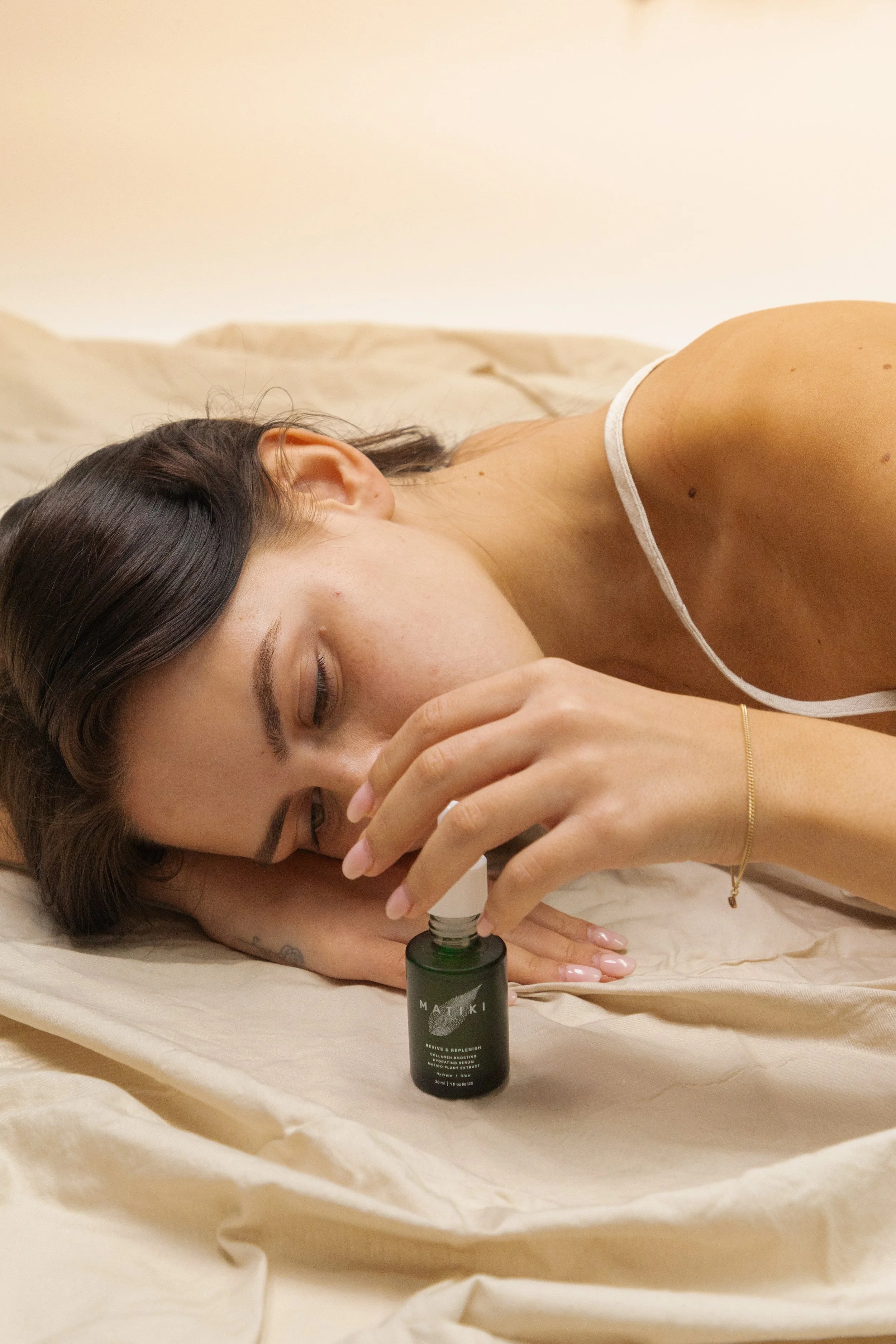 A woman lying on a bed with her eyes closed, holding a small bottle, with a dropper near her face.