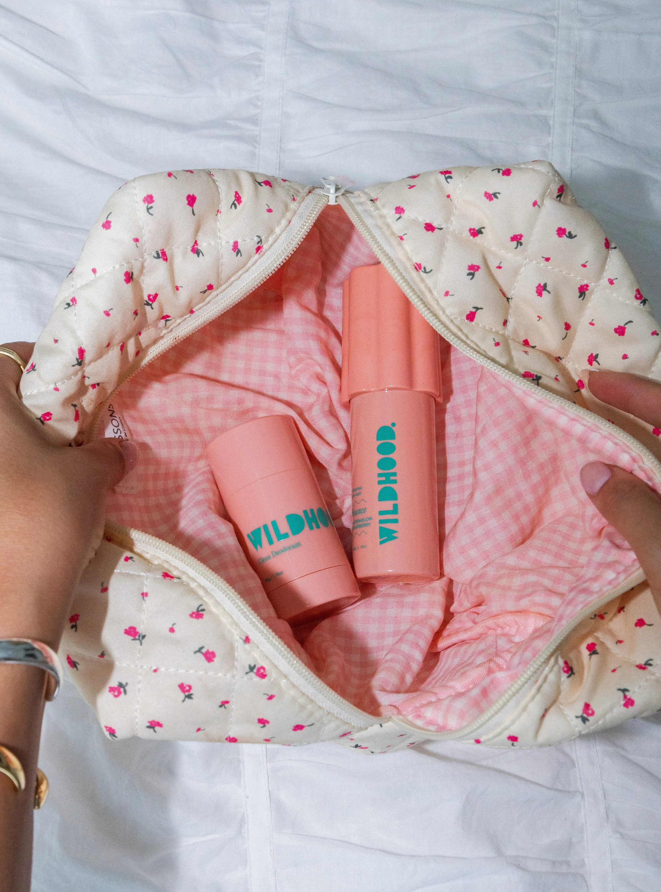 Open floral-patterned bag lined with pink gingham fabric, containing two pink cylindrical containers labeled 'WILDHOP'}