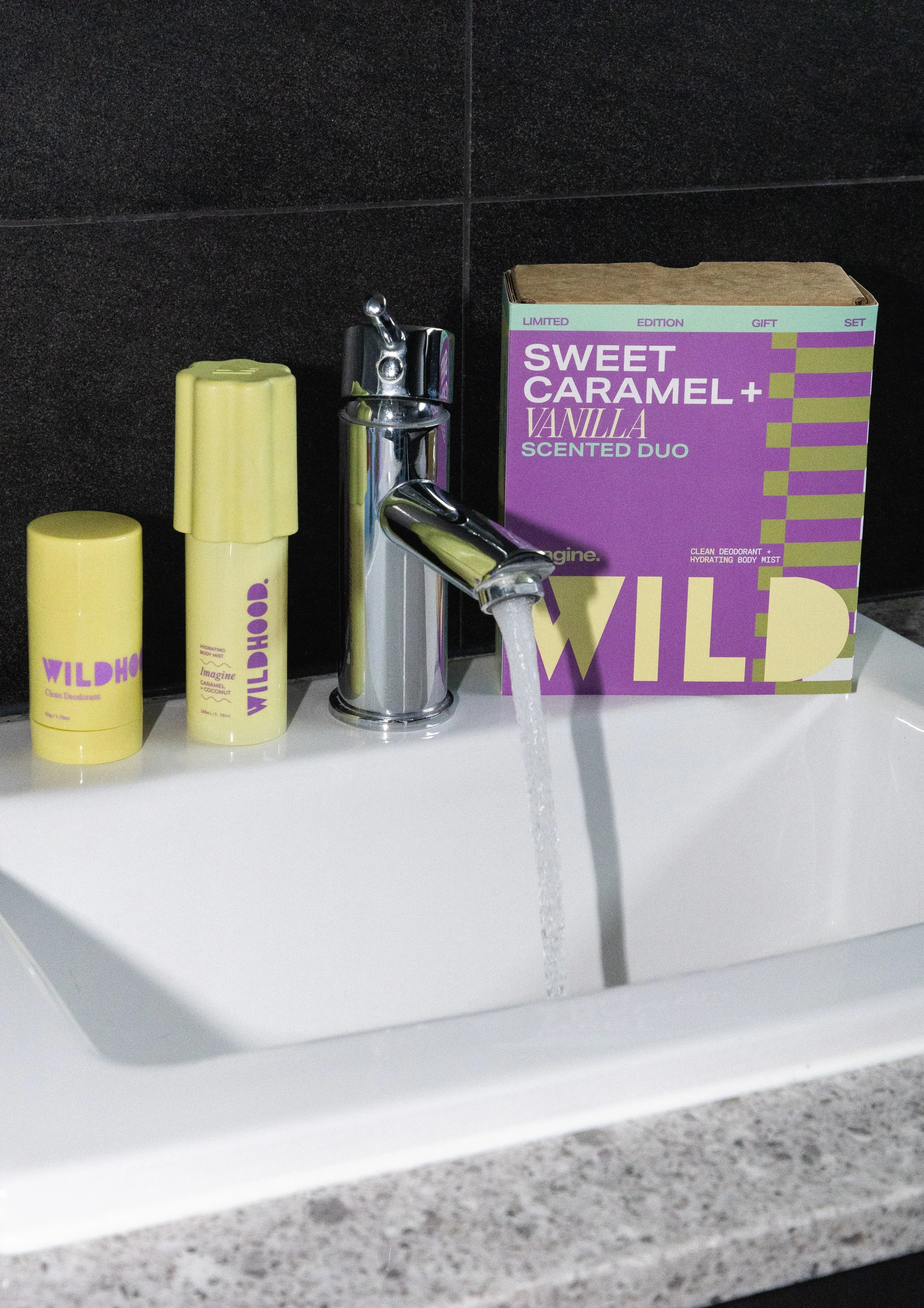 Bathroom sink with yellow Wildhot deodorant, a chrome faucet with water running, and a purple box of Sweet Caramel Vanilla scented body spray.