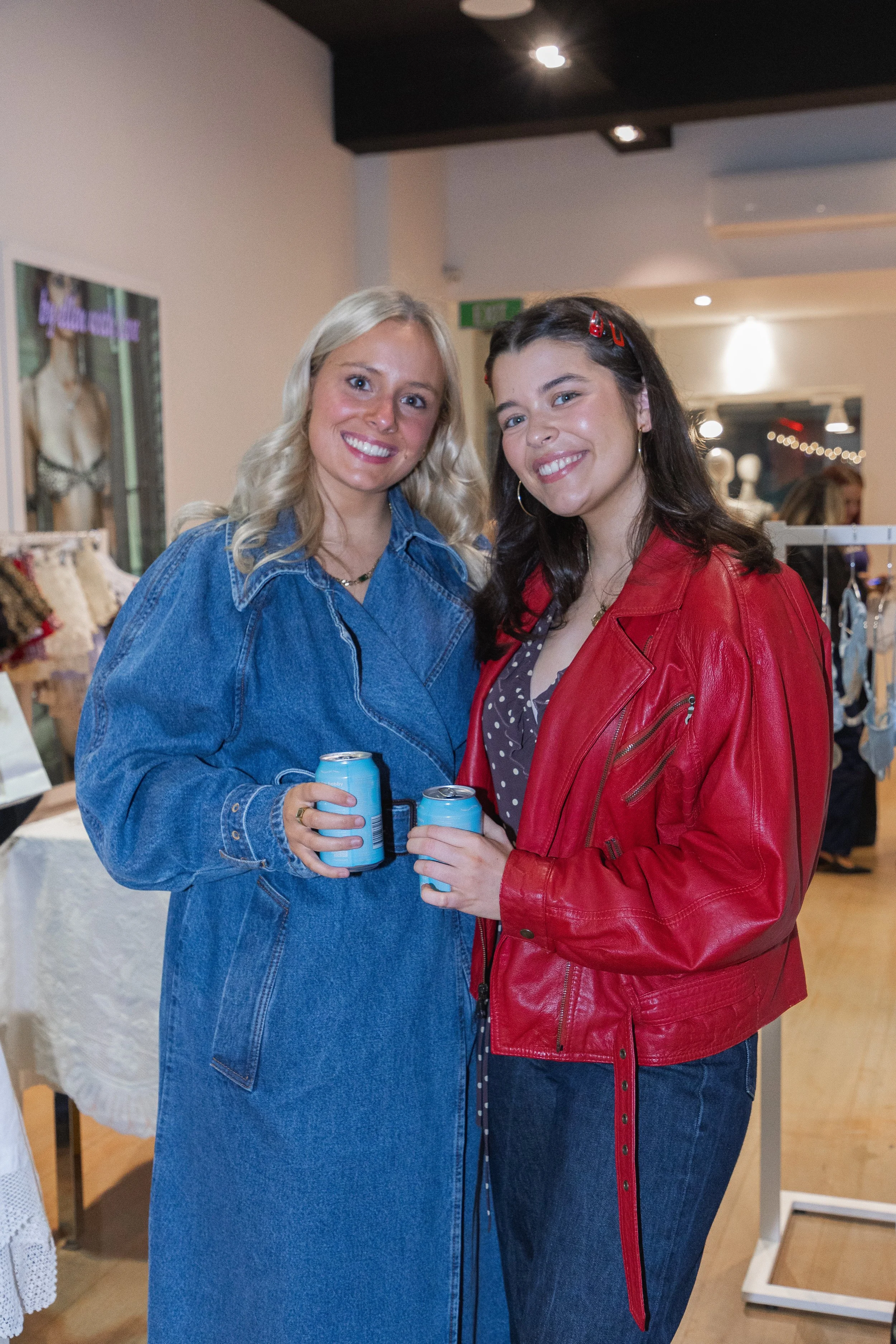 Two women smiling and holding cans at an indoor event or party.