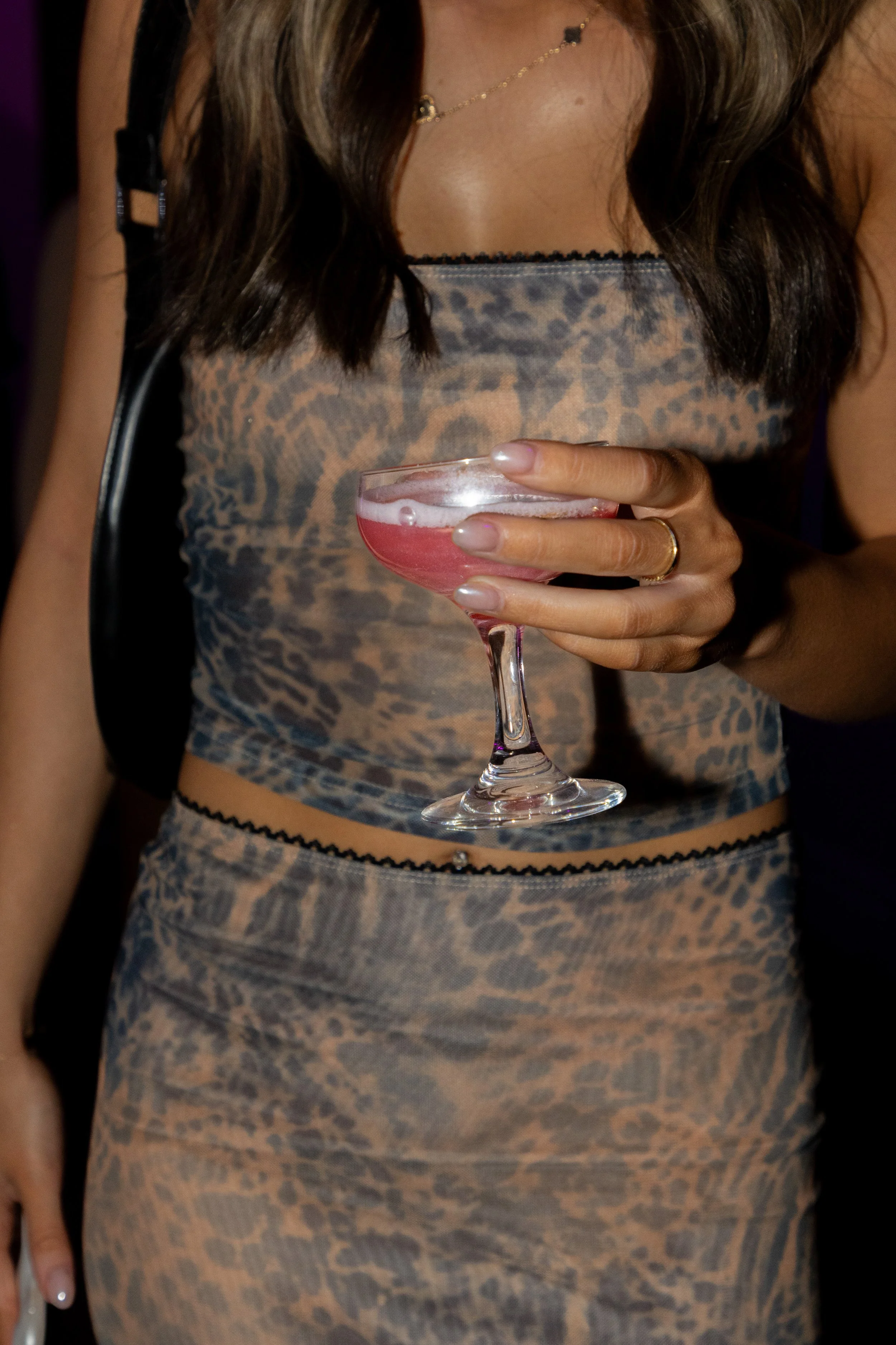 A woman in a leopard print dress holding a pink cocktail glass with a drink inside.