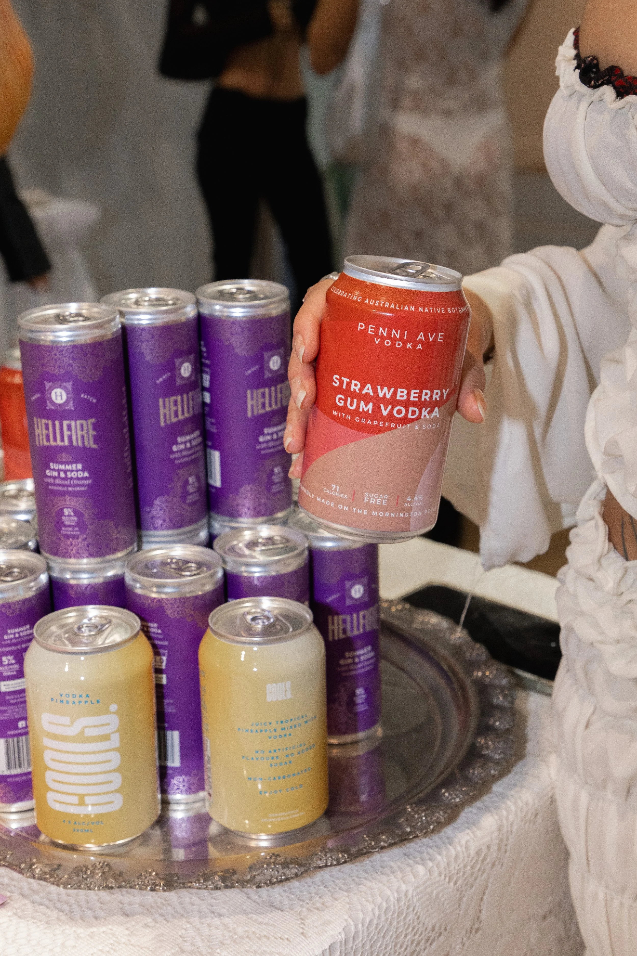 Person holding a can of strawberry gum vodka among cans of Hellfire gin and soda and cans of Bubble vodka on a silver tray.