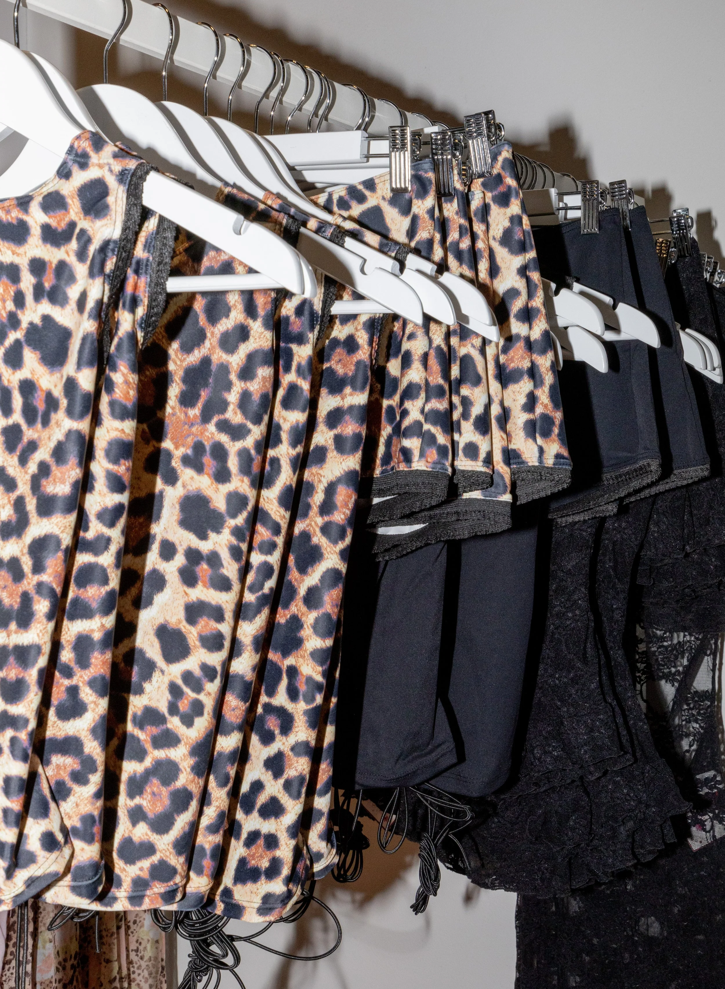Clothing hangs on a rack, featuring leopard print shorts, black shorts, and lace black lingerie.