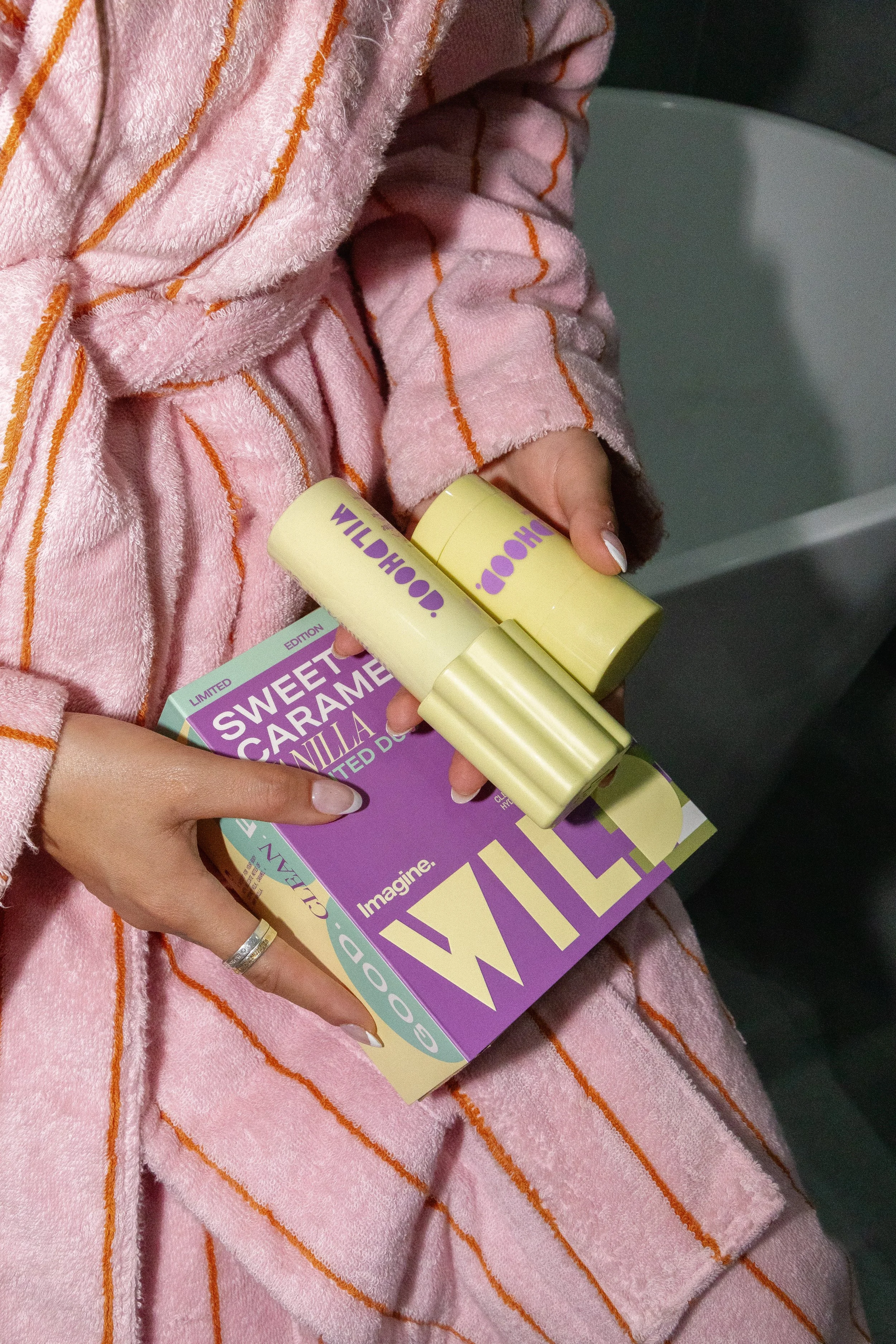 Person wearing a pink striped towel holding a box of gum and two bottles of lip balm.