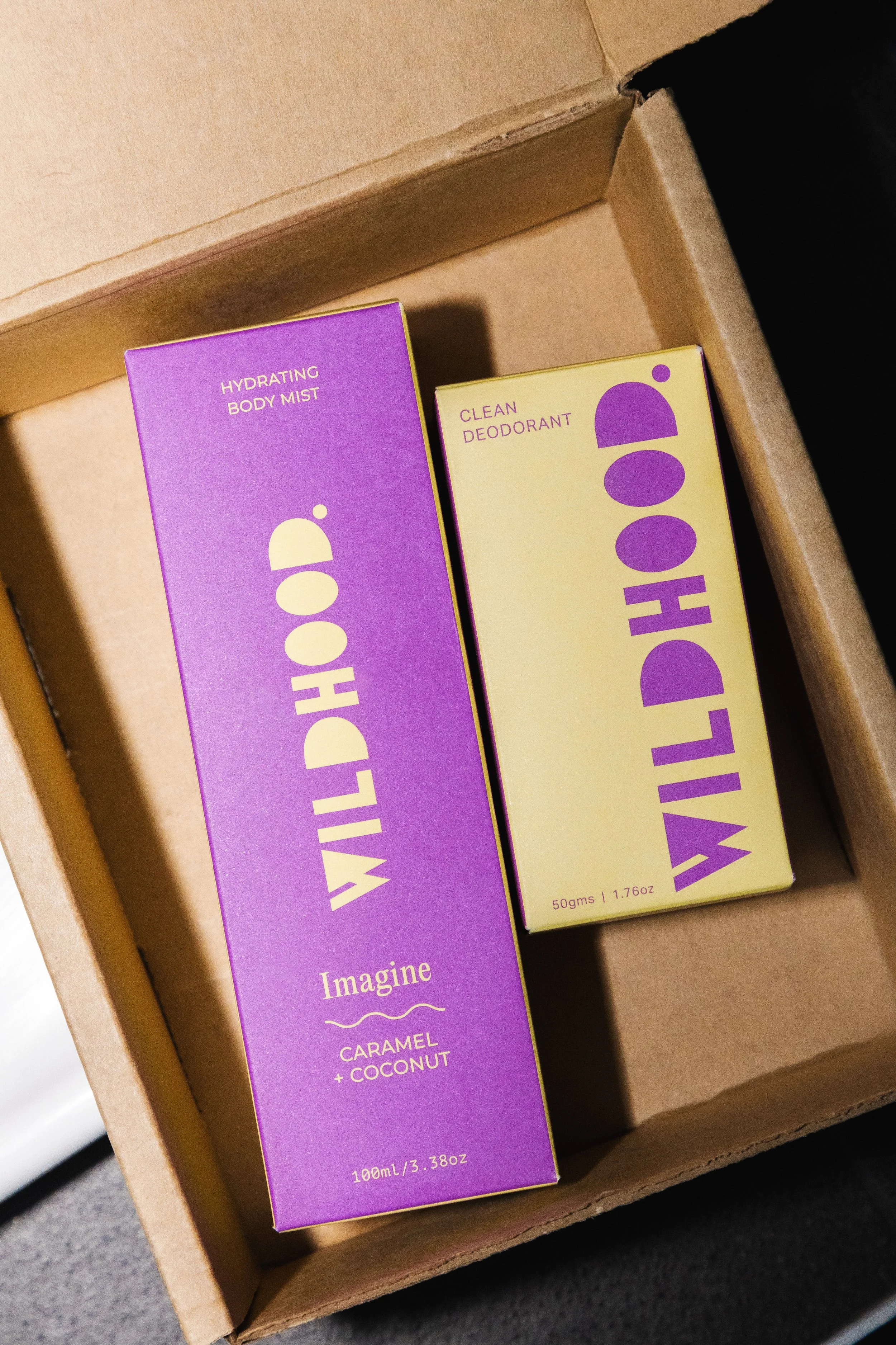 Two Wildthink products inside a cardboard box: one purple box labeled Hydrating Body Mist and one yellow box labeled Clean Deodorant.