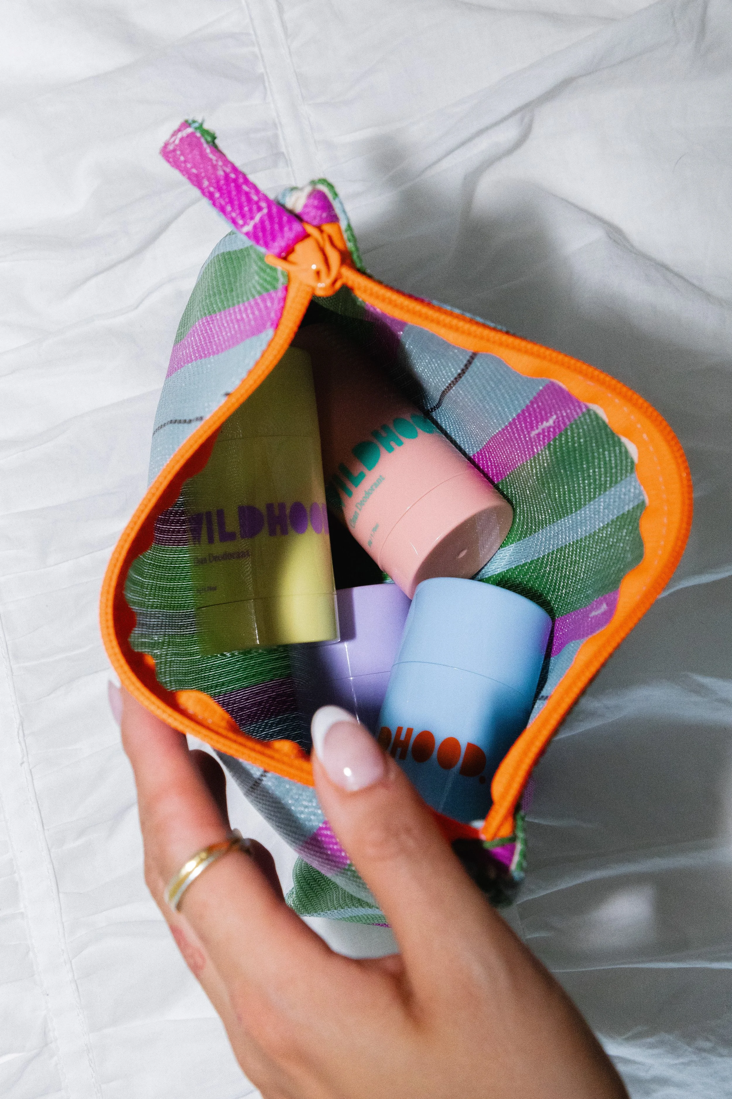 Inside a small colorful bag with Zipper, containing four cylindrical bottles of skincare or cosmetic products in pastel shades of green, pink, blue, and purple.