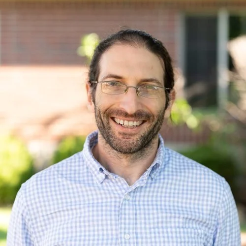 Man smiles at camera in a blue gingham shirt