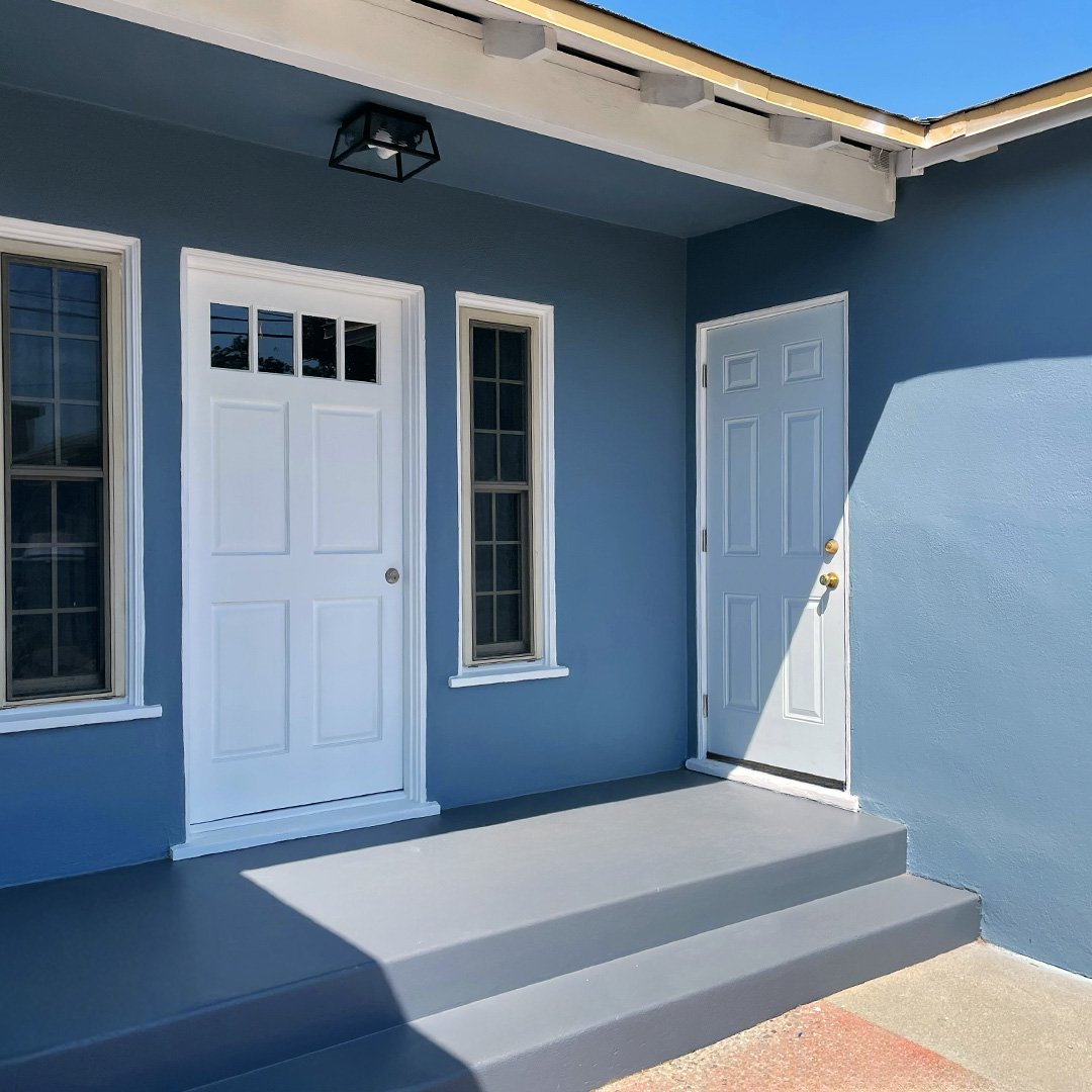 Front porch with two white doors on a blue house wall, with two narrow windows next to each door, gray steps leading up to the doors, and a black outdoor light fixture above.