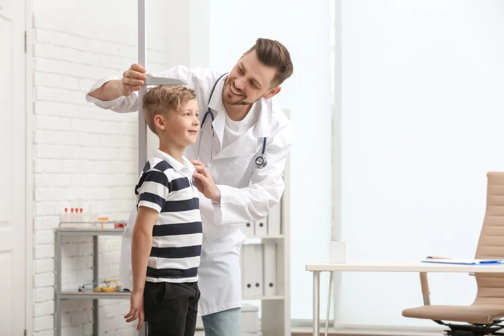 A smiling male doctor talking to a young boy in a medical office.