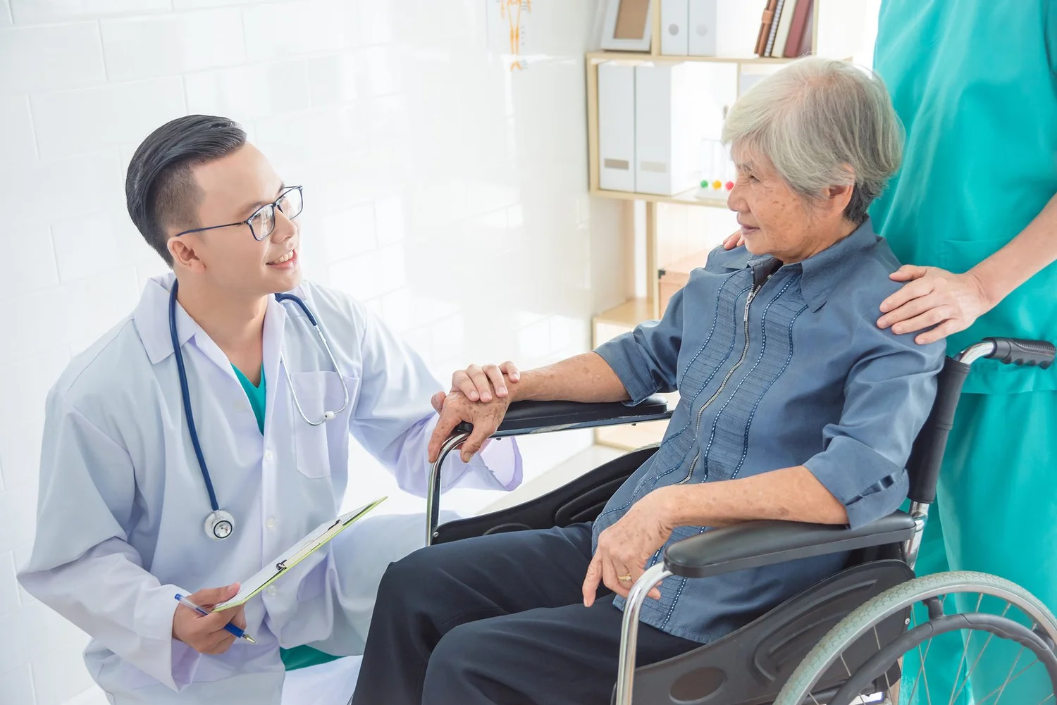 A doctor smiling at an older woman in a wheelchair with a caregiver