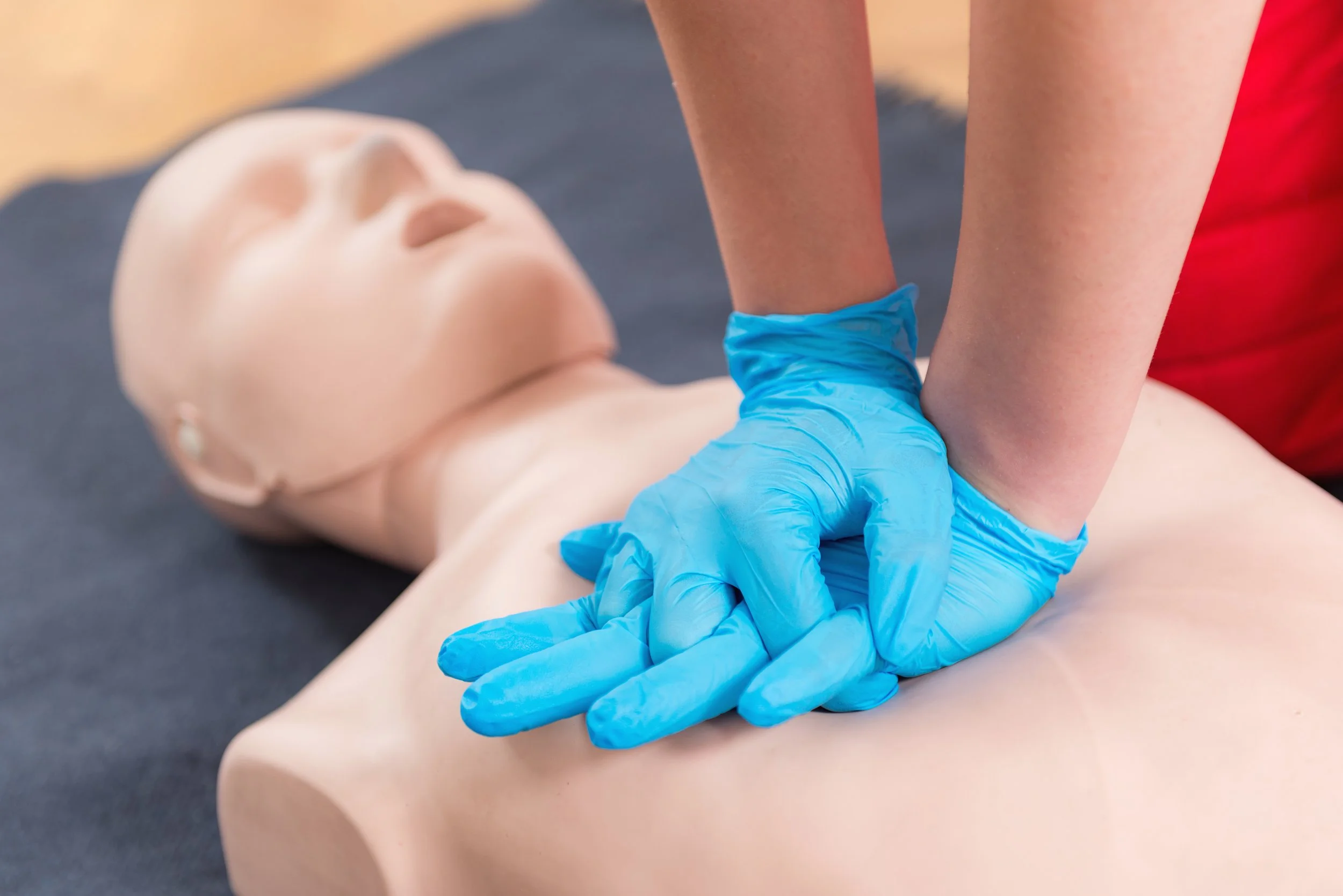A person wearing blue gloves performing chest compressions on a CPR training mannequin.  CPR training through XCOM Security Group's Xtra Life Division.