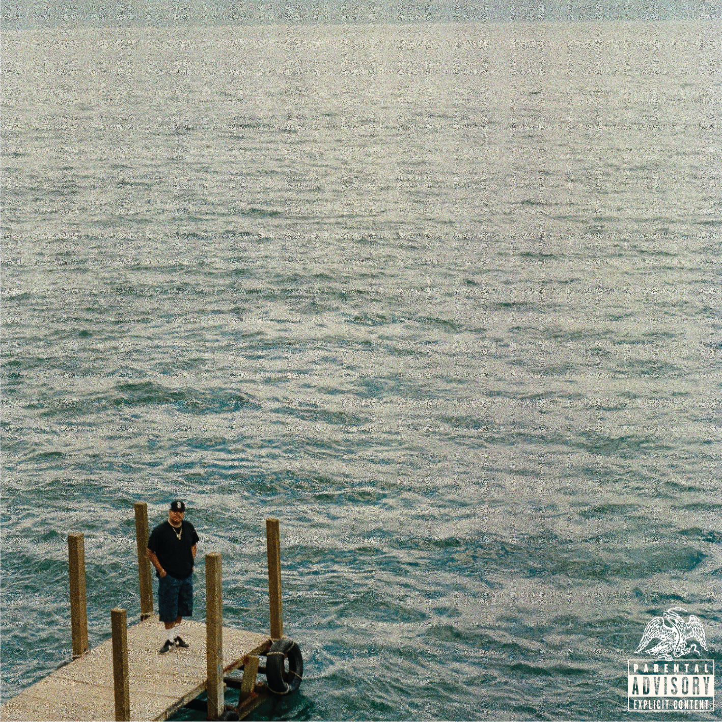 Man standing on a small dock extending into a large body of water, with wooden posts along the dock, overcast sky, and ocean waves in the background.