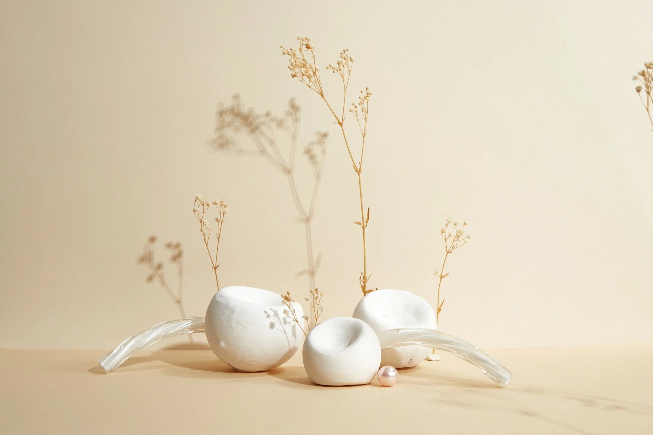 Minimalist arrangement of white ceramic vases with dried flowers on a beige background.