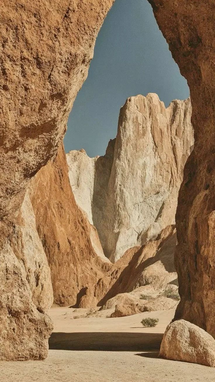 Enter the portal of your heart and soul. A desert landscape with large rock formations and sandy ground, viewed through a natural rock arch.
