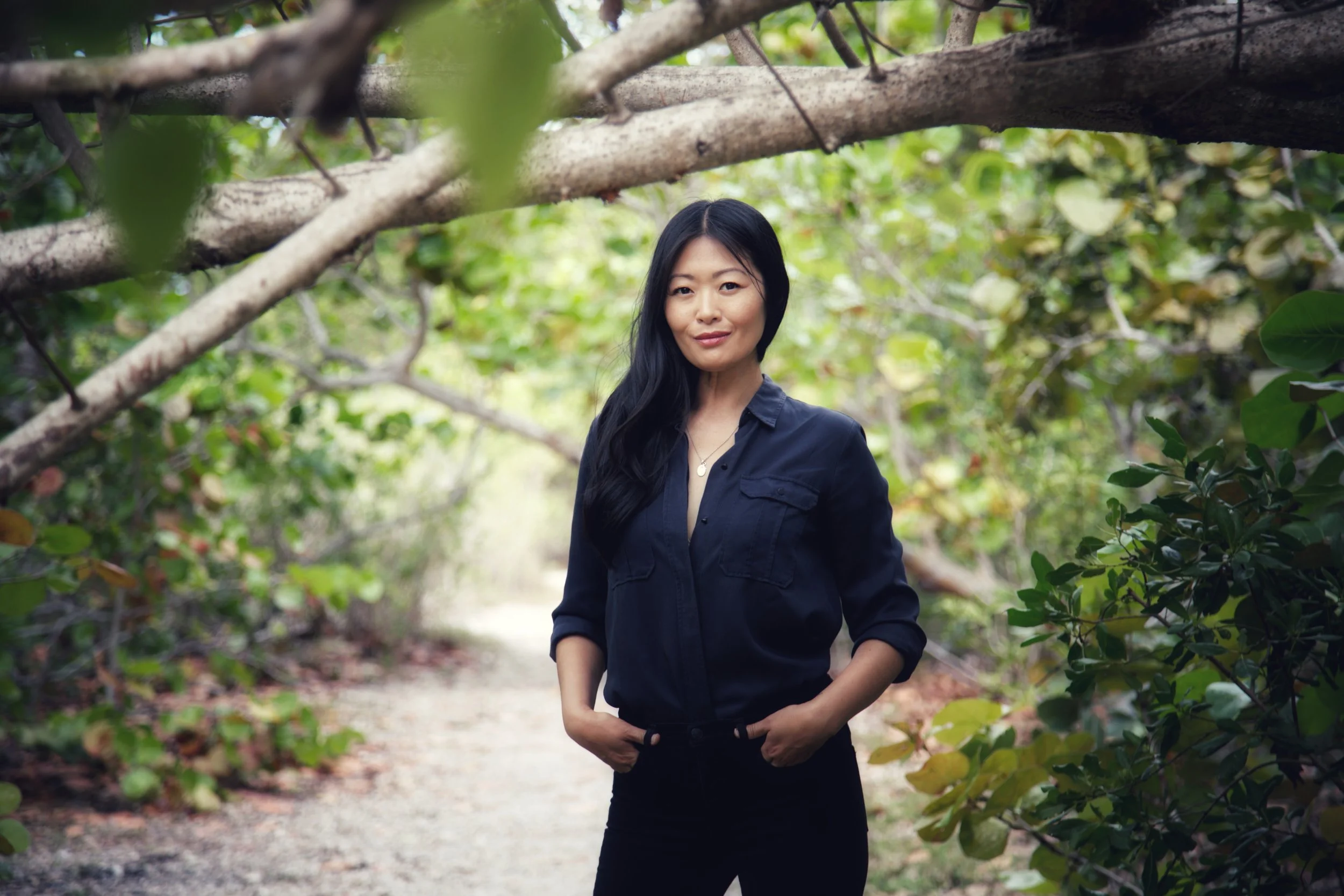 Eunice, a powerfully psychic, intuitive woman, standing in nature of a wooded area with green foliage and trees around her. Omnilove