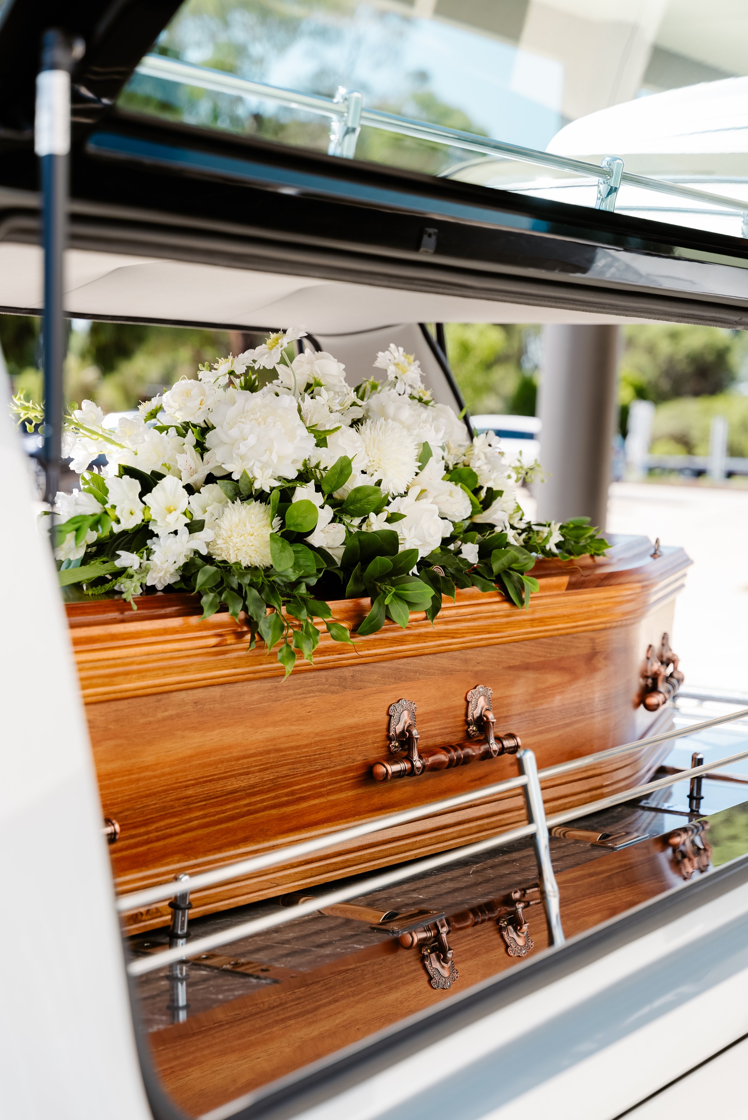 Coffin with white flowers in a hearse trunk