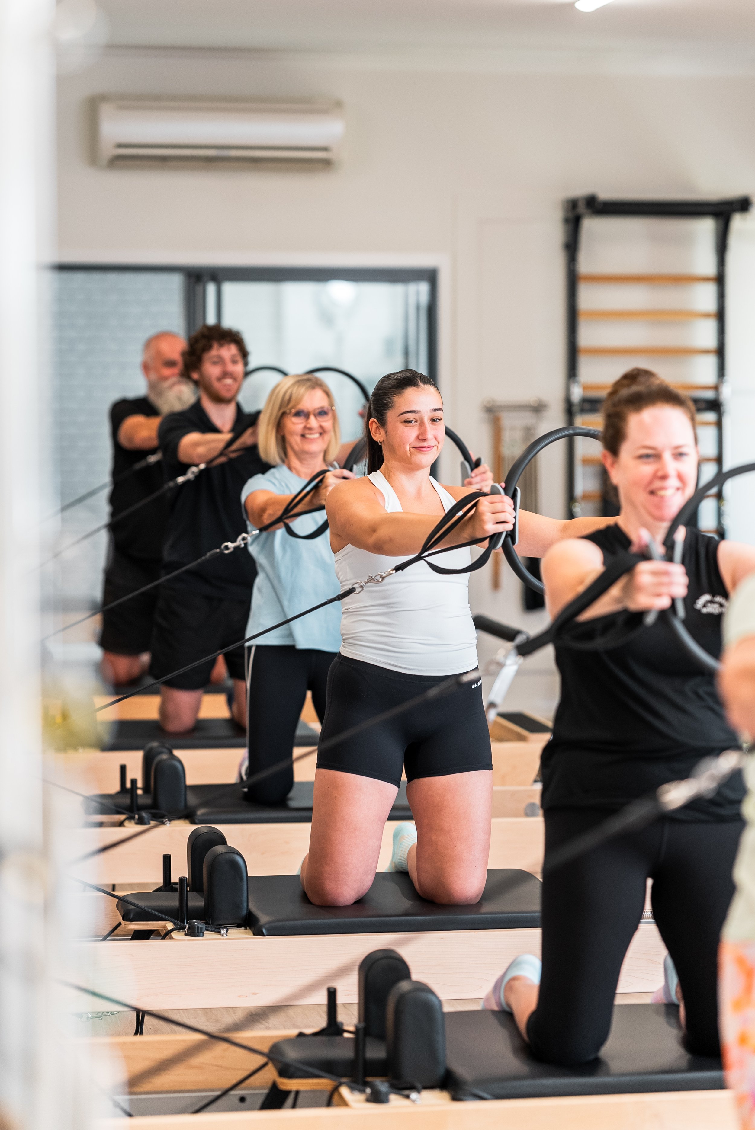 Group of people doing Pilates on reformer machines in a fitness studio.