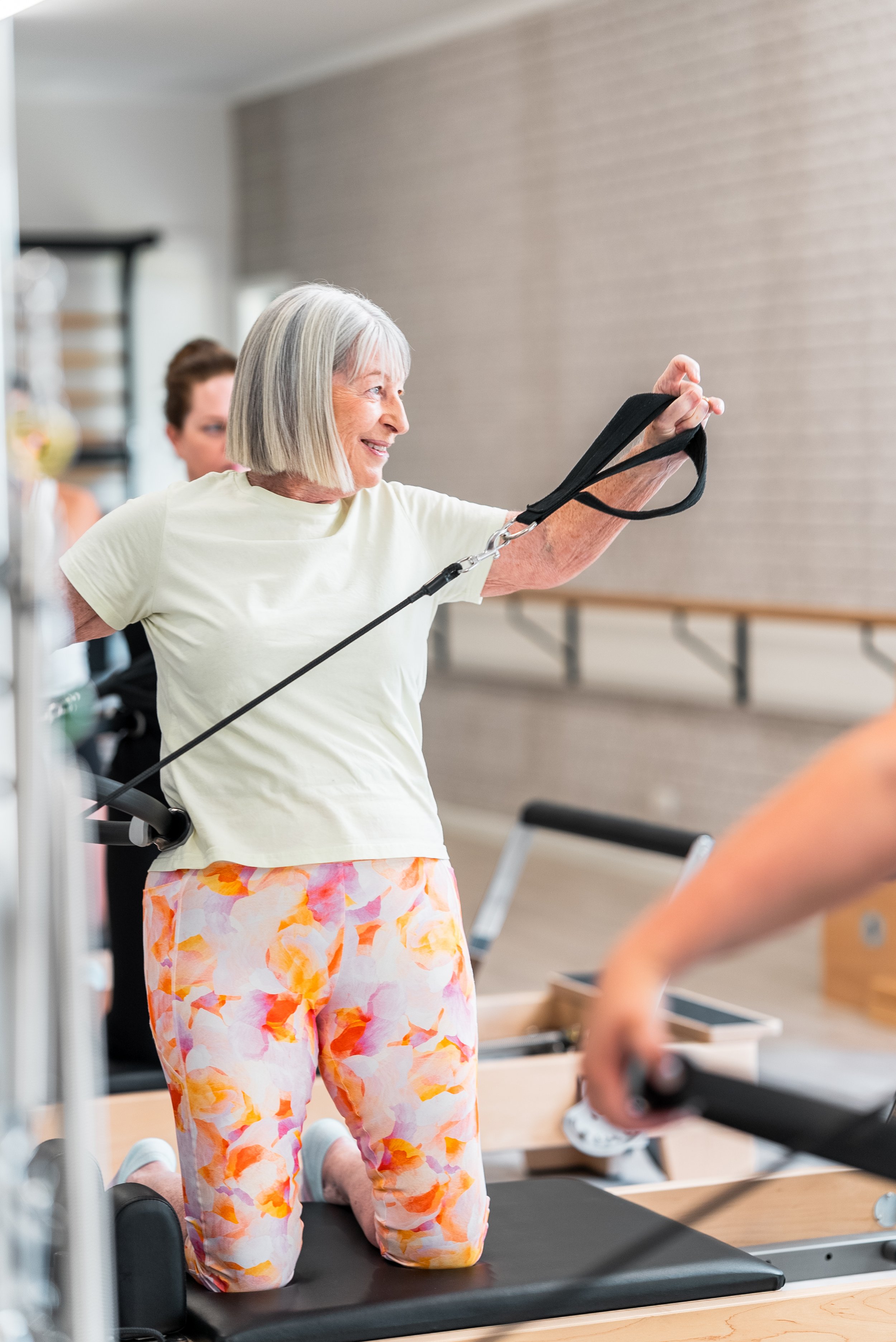 Older woman exercising on a Pilates reformer in a fitness studio.