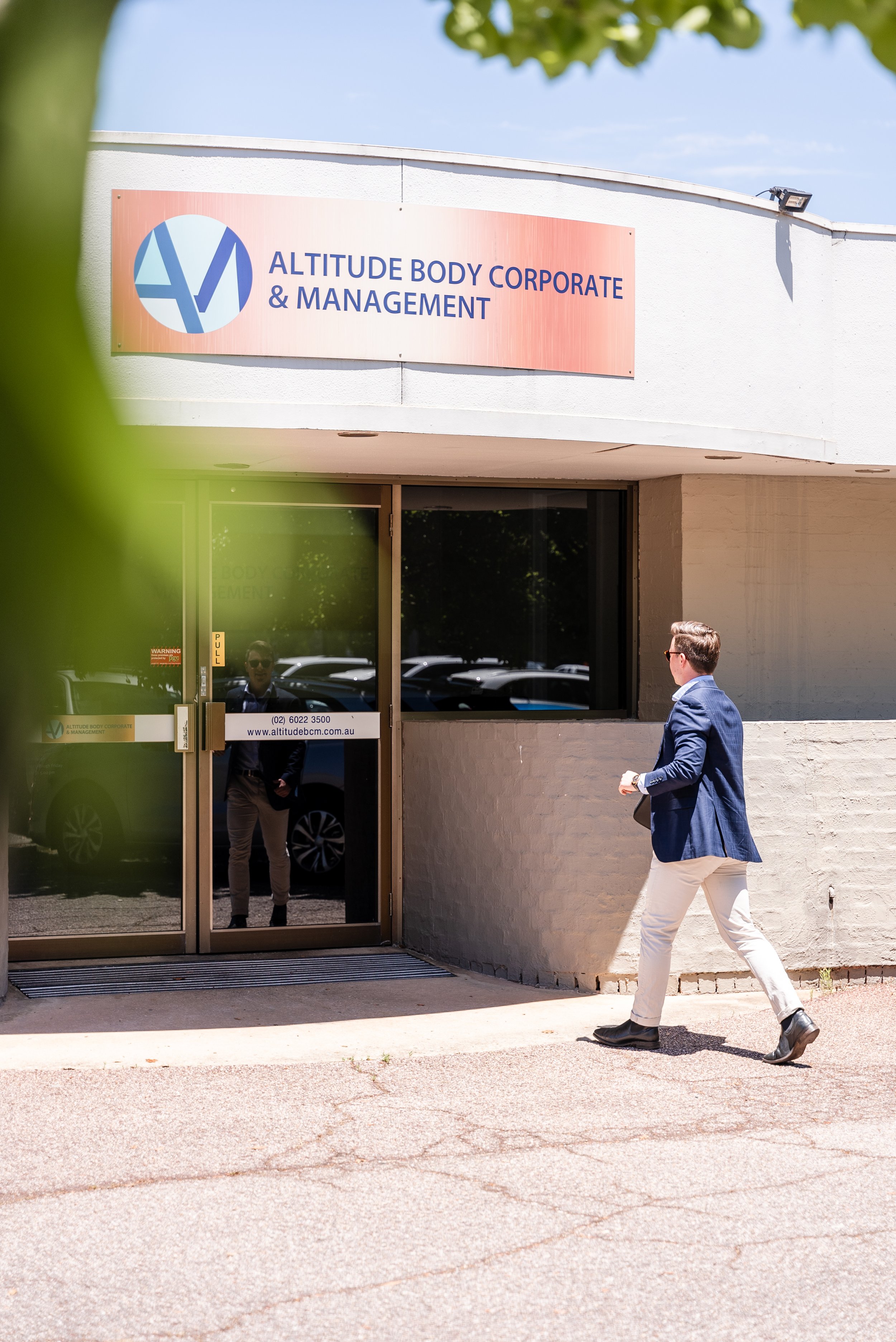 Man approaching entrance of Altitude Body Corporate & Management office, with sign displaying the company name and logo above the door.