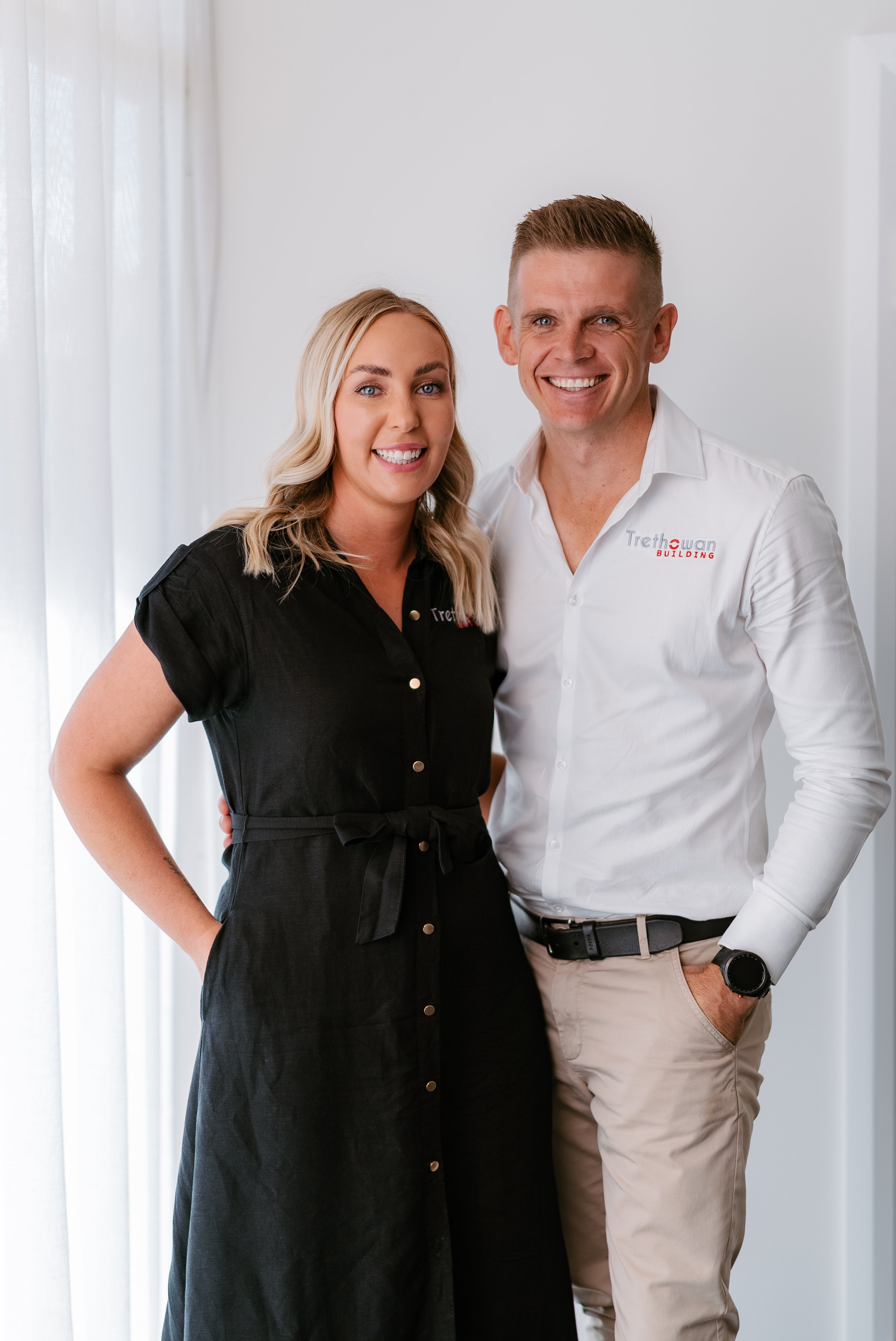 Two people smiling, one wearing a black dress and the other a white shirt with "Trethowan Building" logo.