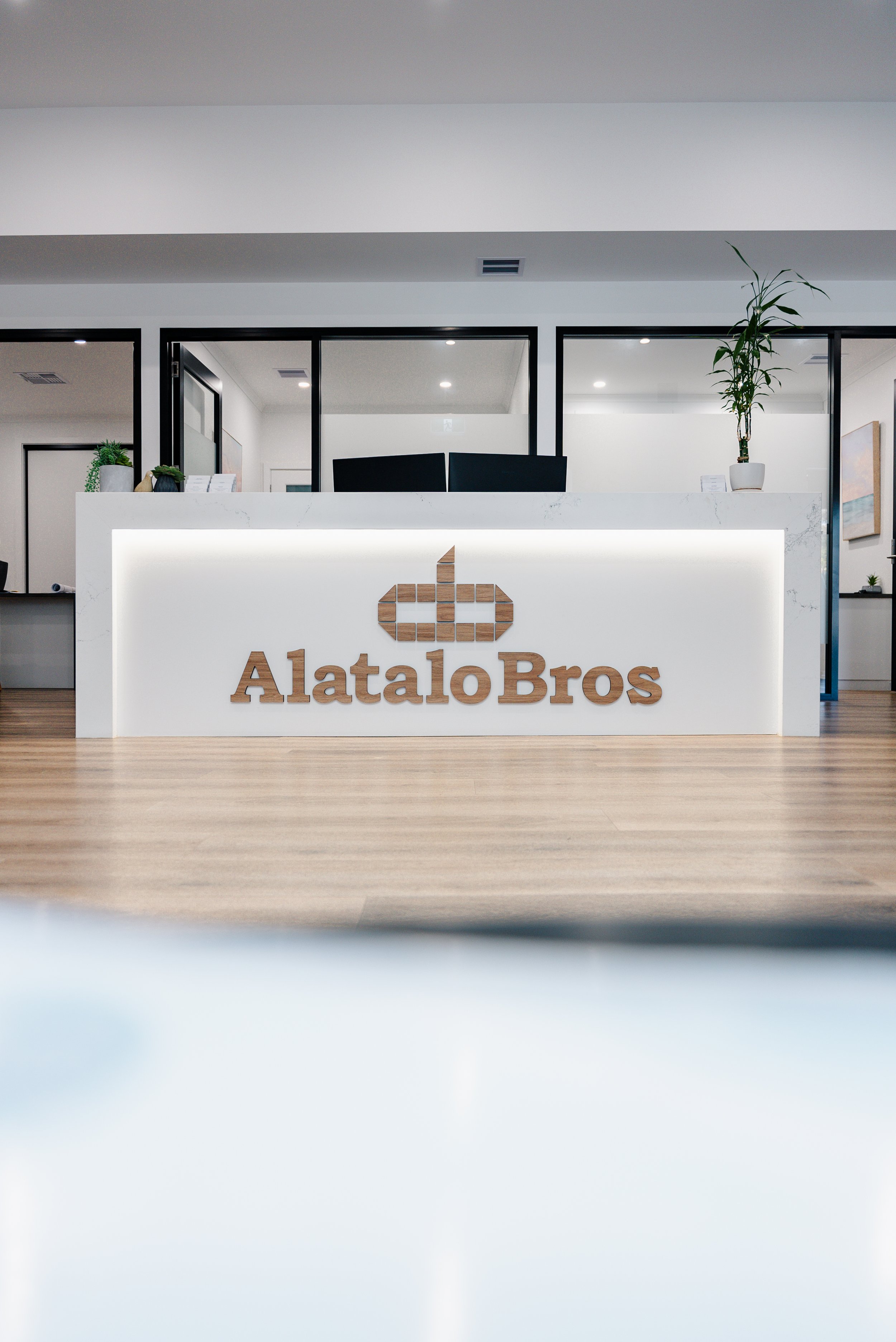 Reception area with "Alatalo Bros" logo on a white desk, indoor plants, and modern office decor.