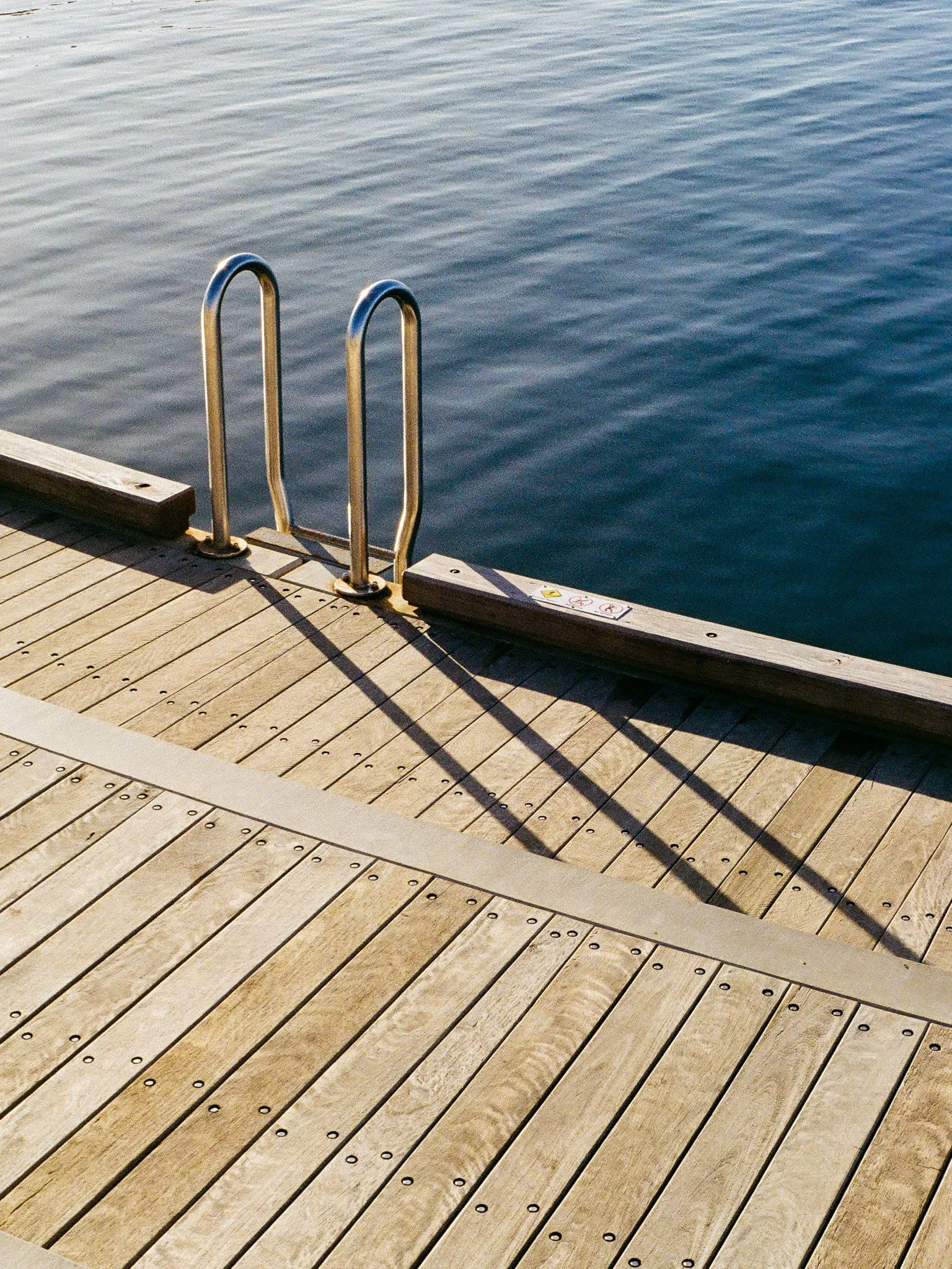 A wooden dock with a metal ladder leading into a calm body of water.