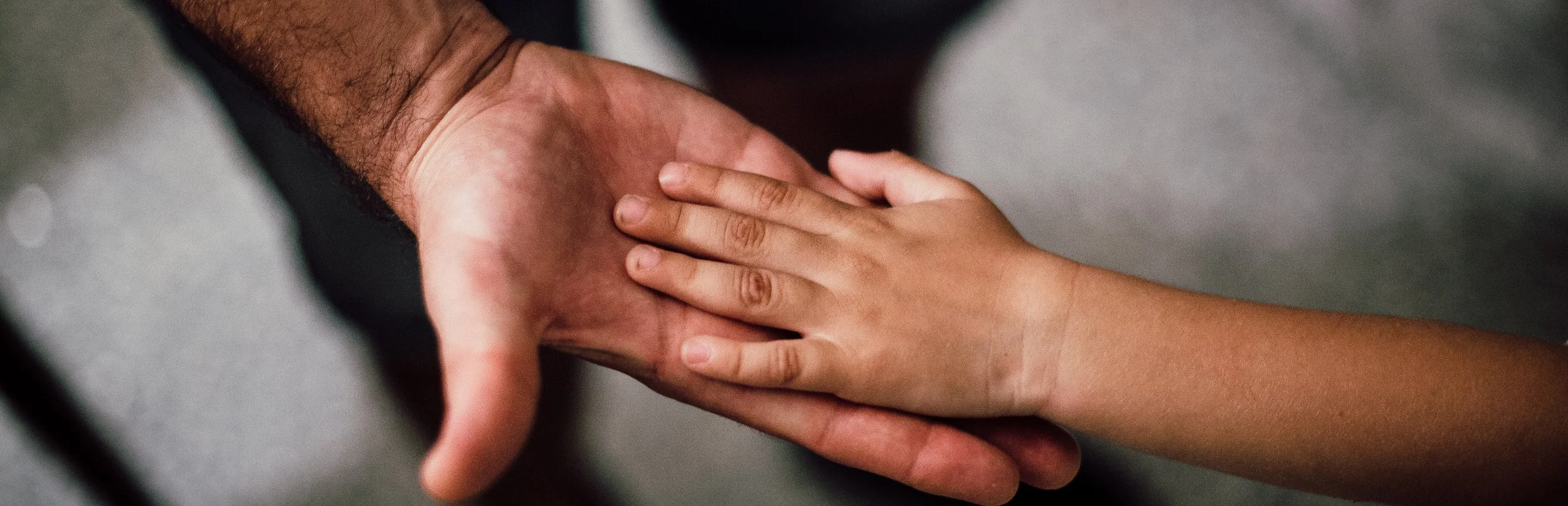 Un bambino che si stringe nel palmo della mano di un adulto.