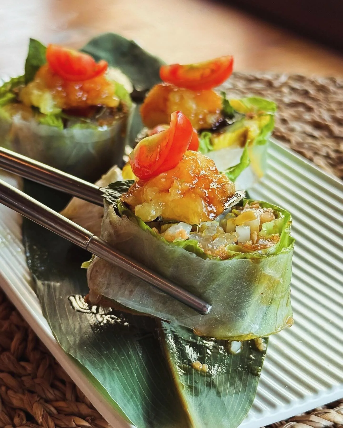 新鮮的春捲特寫，上面鋪著切碎的番茄和醬汁，盛放在白色的長方形盤子上。