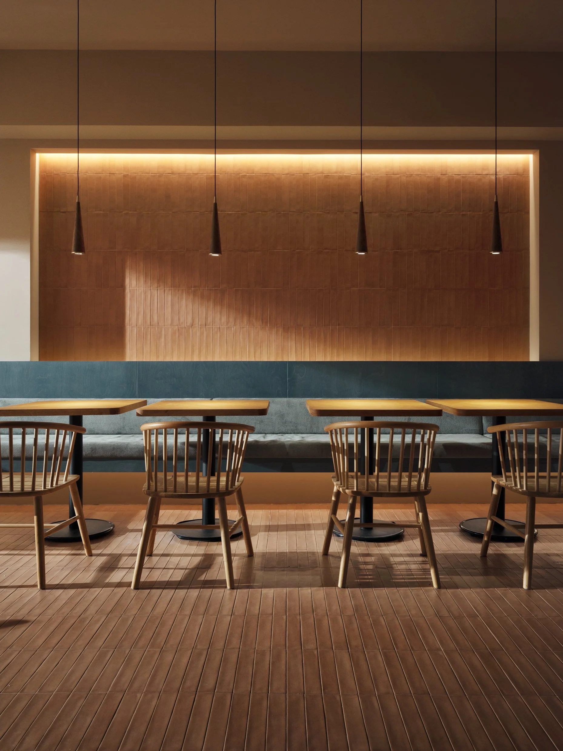 一間空蕩蕩的餐廳，擺著木製桌椅、有軟墊長椅和吊燈，呈現現代風格的室內設計。