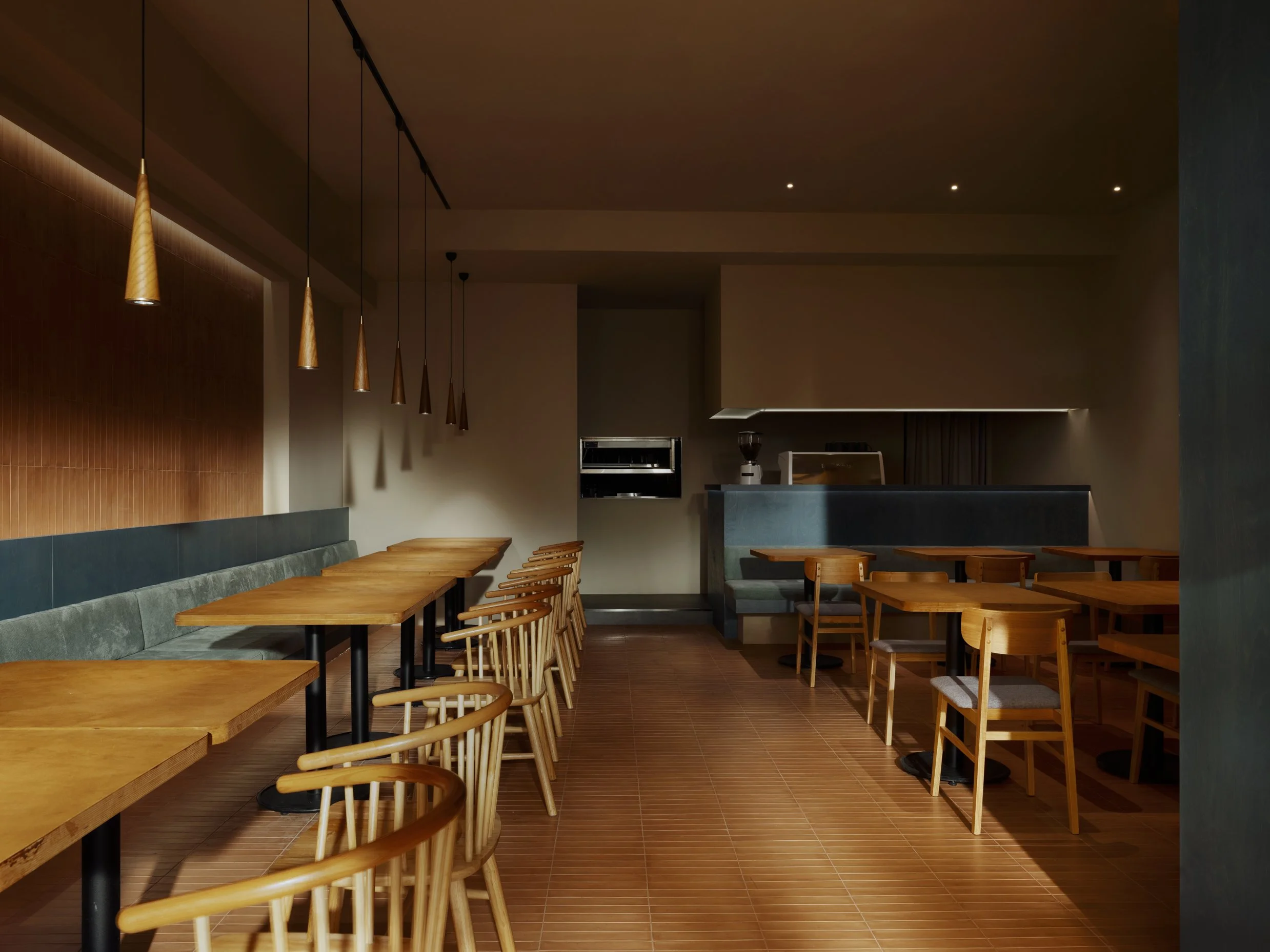 Empty modern cafe interior with wooden tables and chairs, pendant lights, and warm lighting.