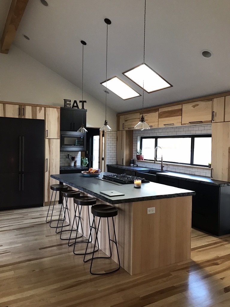 Modern kitchen with wooden cabinets, black countertops, island with bar stools, pendant lights, and skylights.