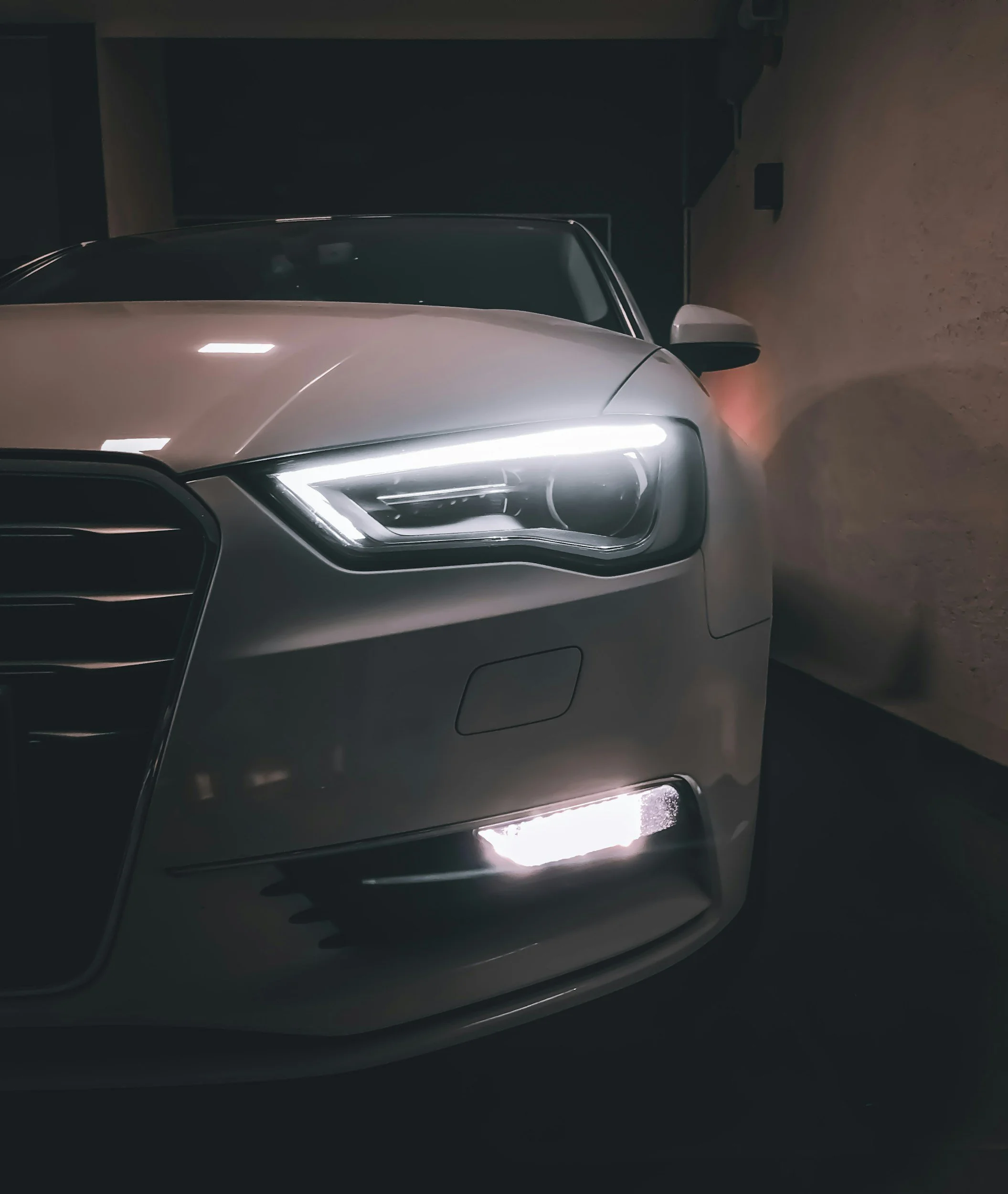 Voiture blanche garée dans un parking, vue de face avec phares allumés.