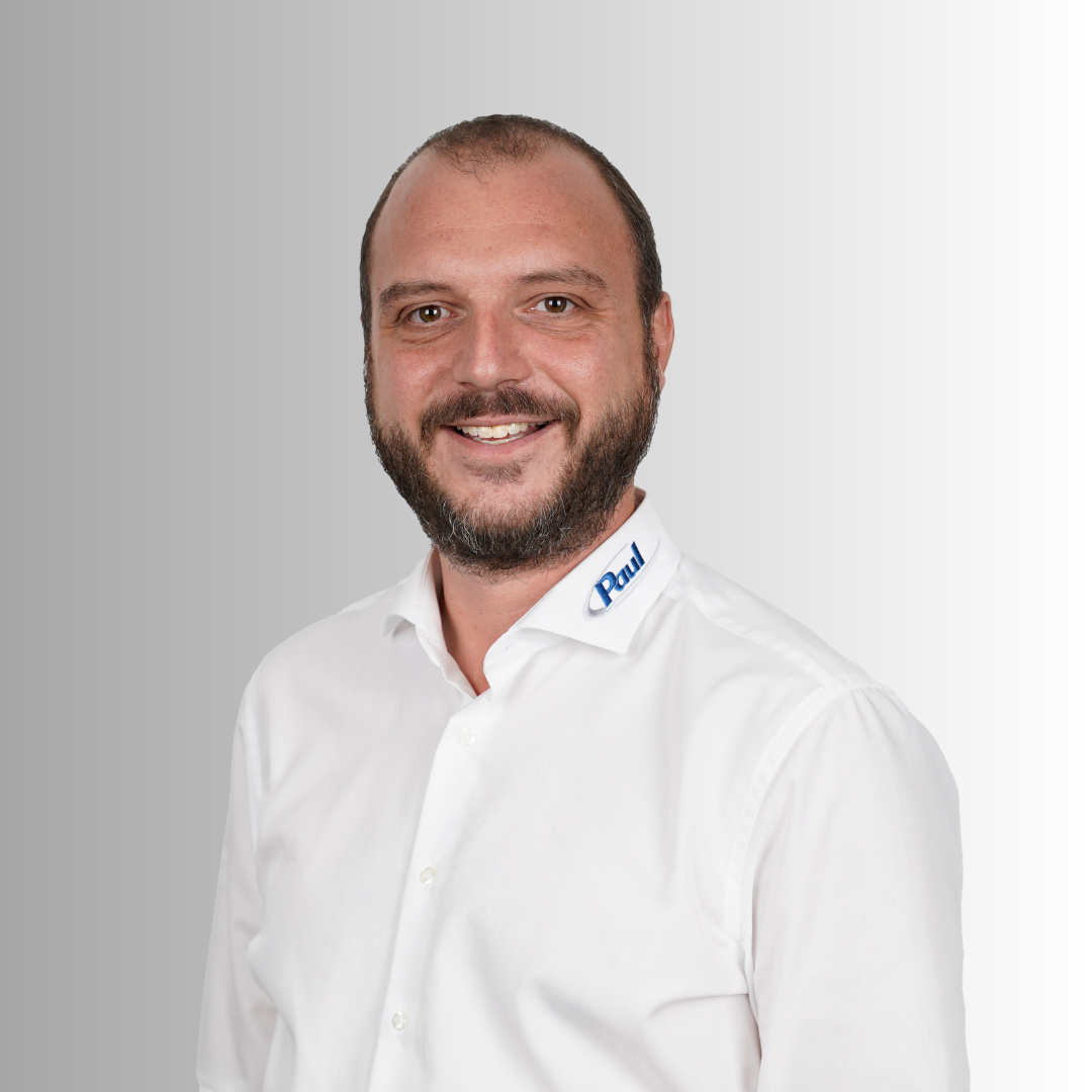 Porträt eines lächelnden Mannes mit braunem Bart, kurzen Haaren und weißem Hemd mit Logo auf der Kragen.