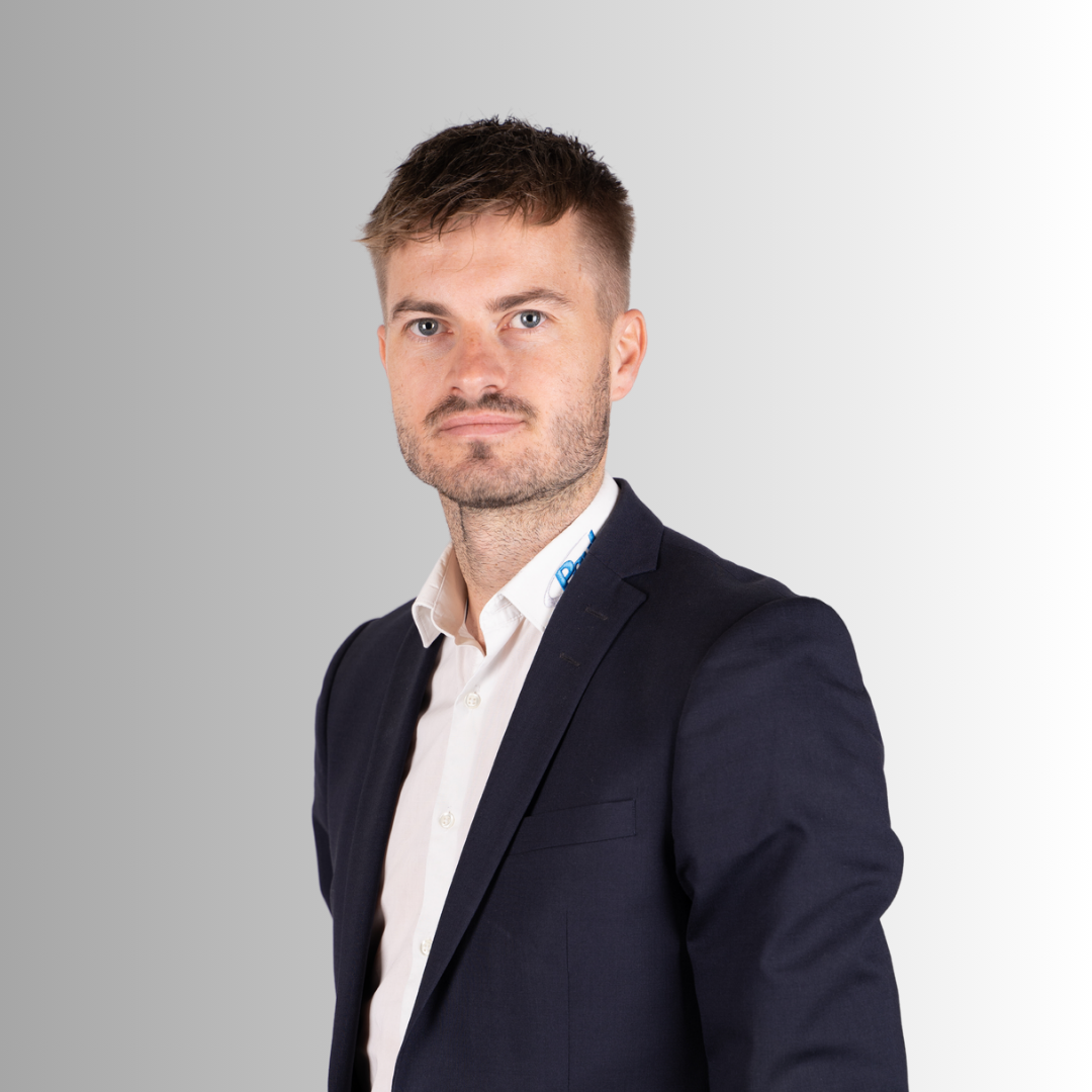 Junge Mann in dunklem Anzug und weißem Hemd gegen grauen Hintergrund.