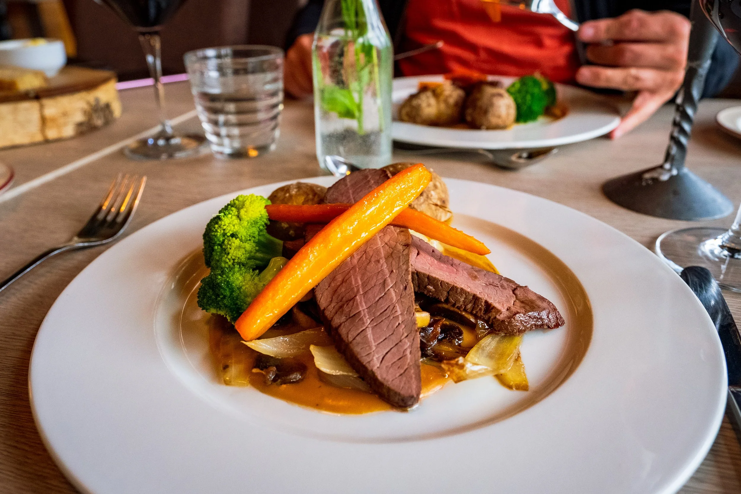 Steik med grønnsaker og poteter på en hvit tallerken på et middagsbord.